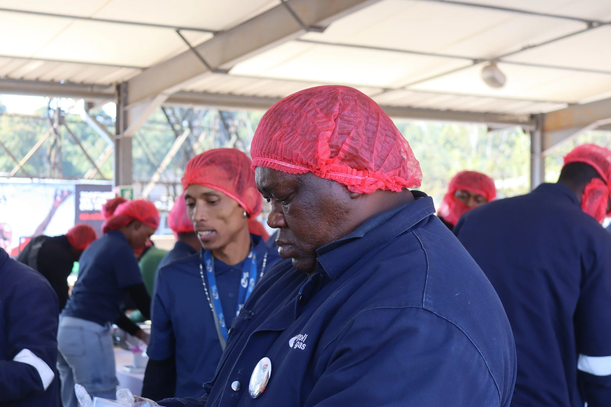 Group of people working together at an outdoor event, wearing red hairnets and dark blue uniforms.