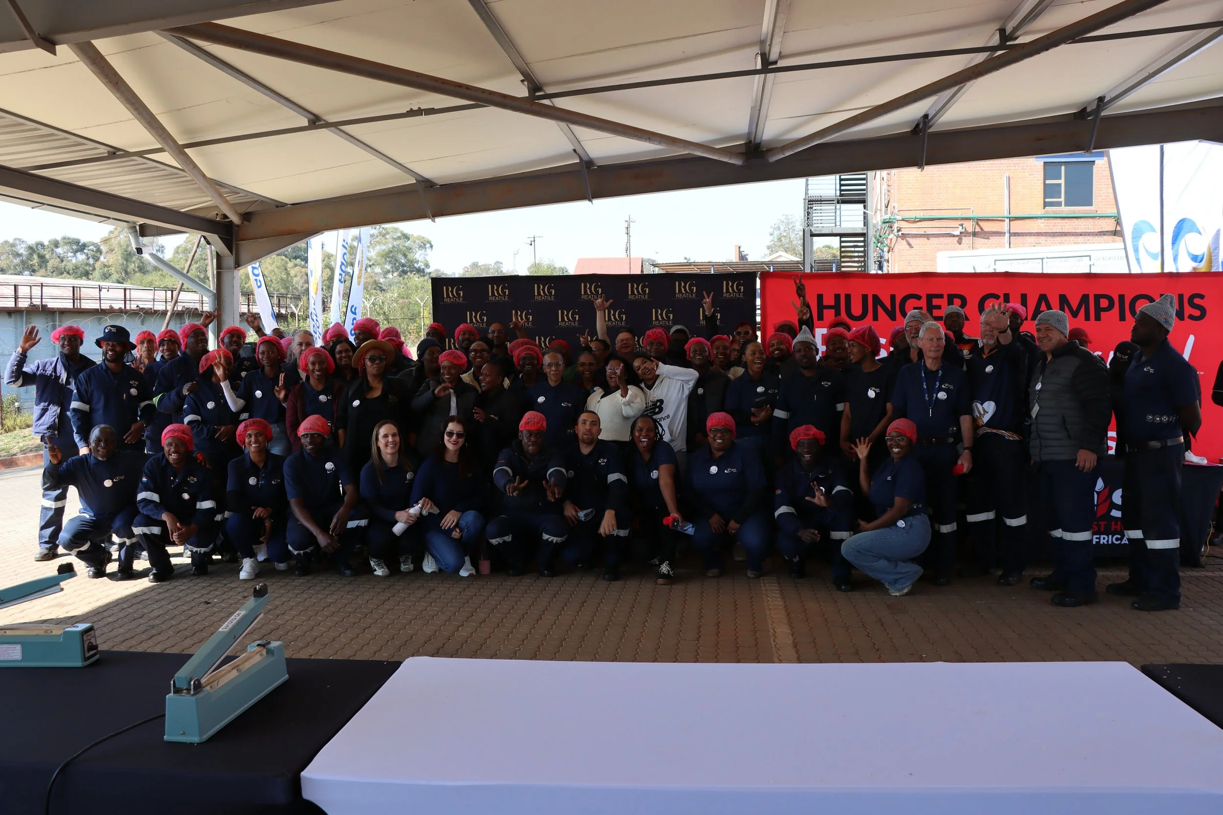 Group of people posing under a canopy with banners behind them that read 'HUNGER CHAMPIONS'.