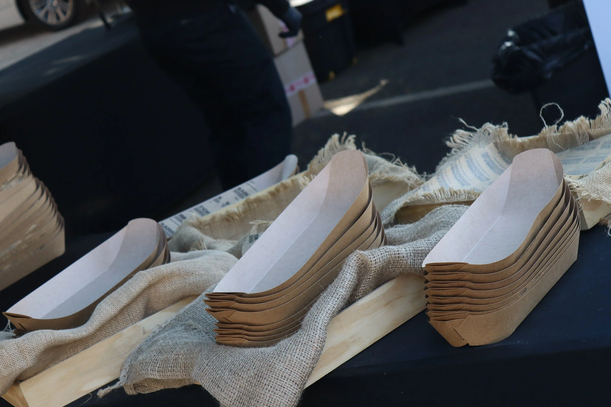 Close-up of an art or craft project involving cardboard, fabric, and paper, with a person standing nearby.
