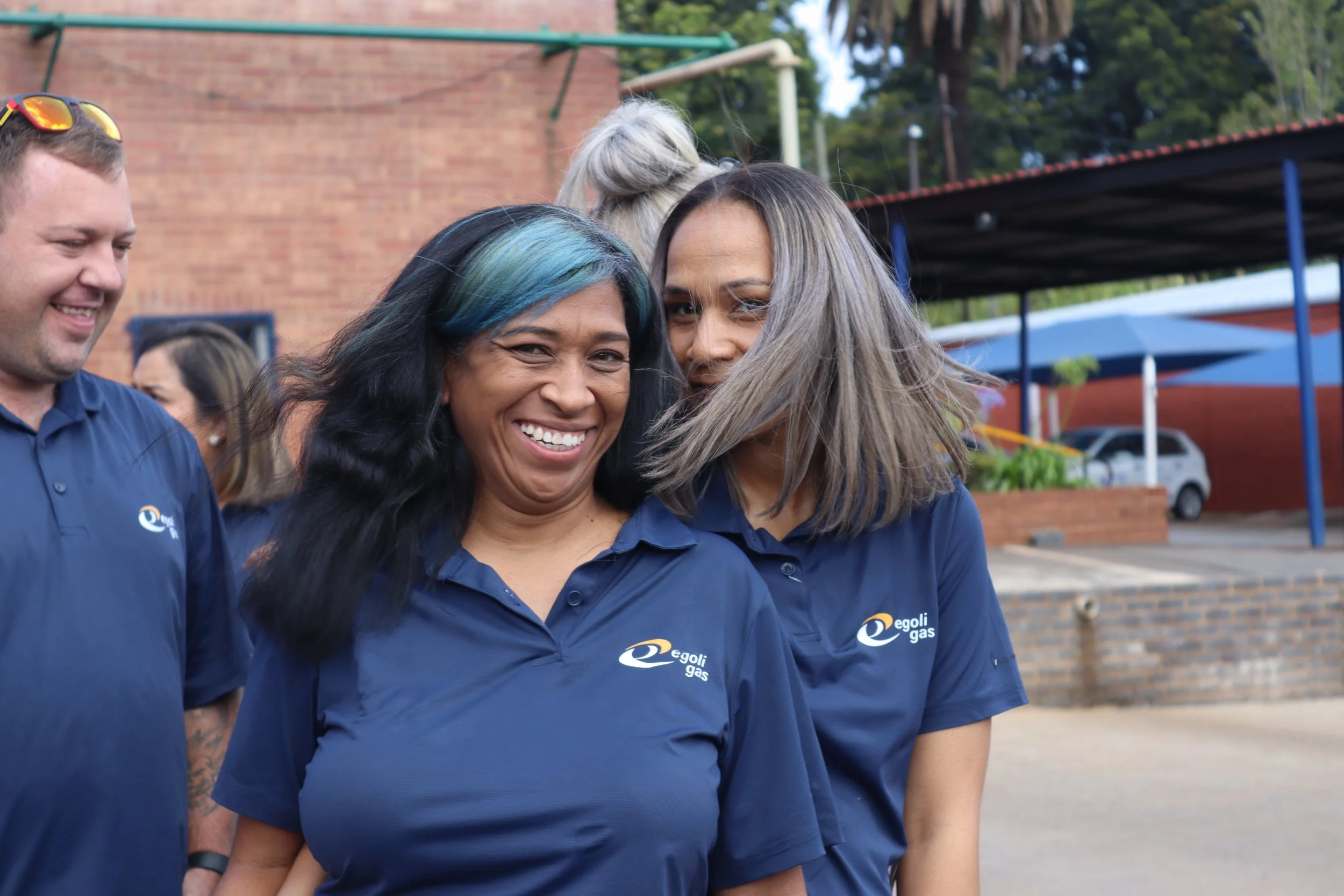 Group of four people smiling outdoors, wearing blue shirts with 'Egoli Gas' logo.