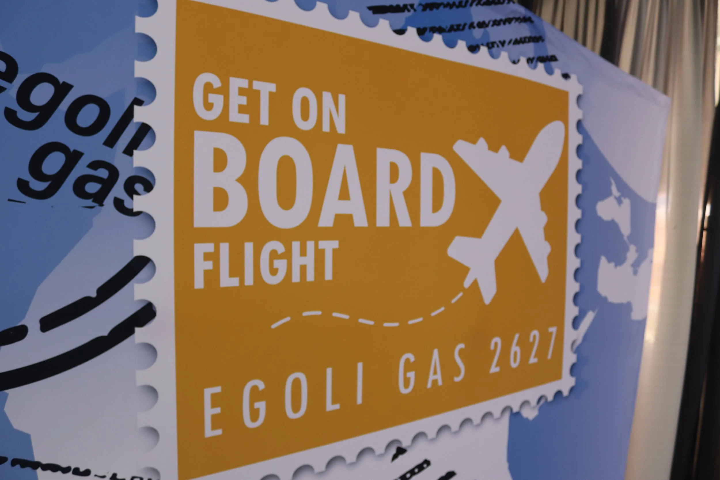 A stamp-shaped sign with the text "Get on Board", showing a silhouette of a person with luggage, and featuring lemon illustrations on a yellow background.