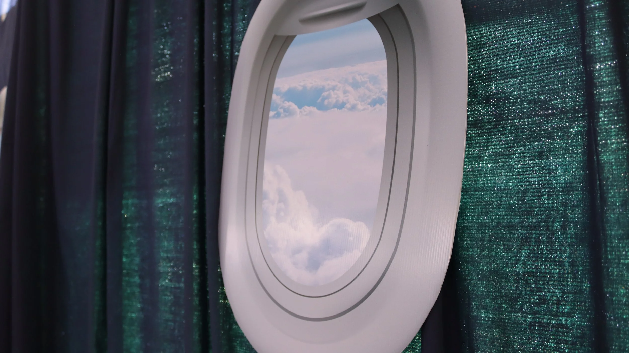 View through airplane window showing clouds and sky, with dark curtains on either side.