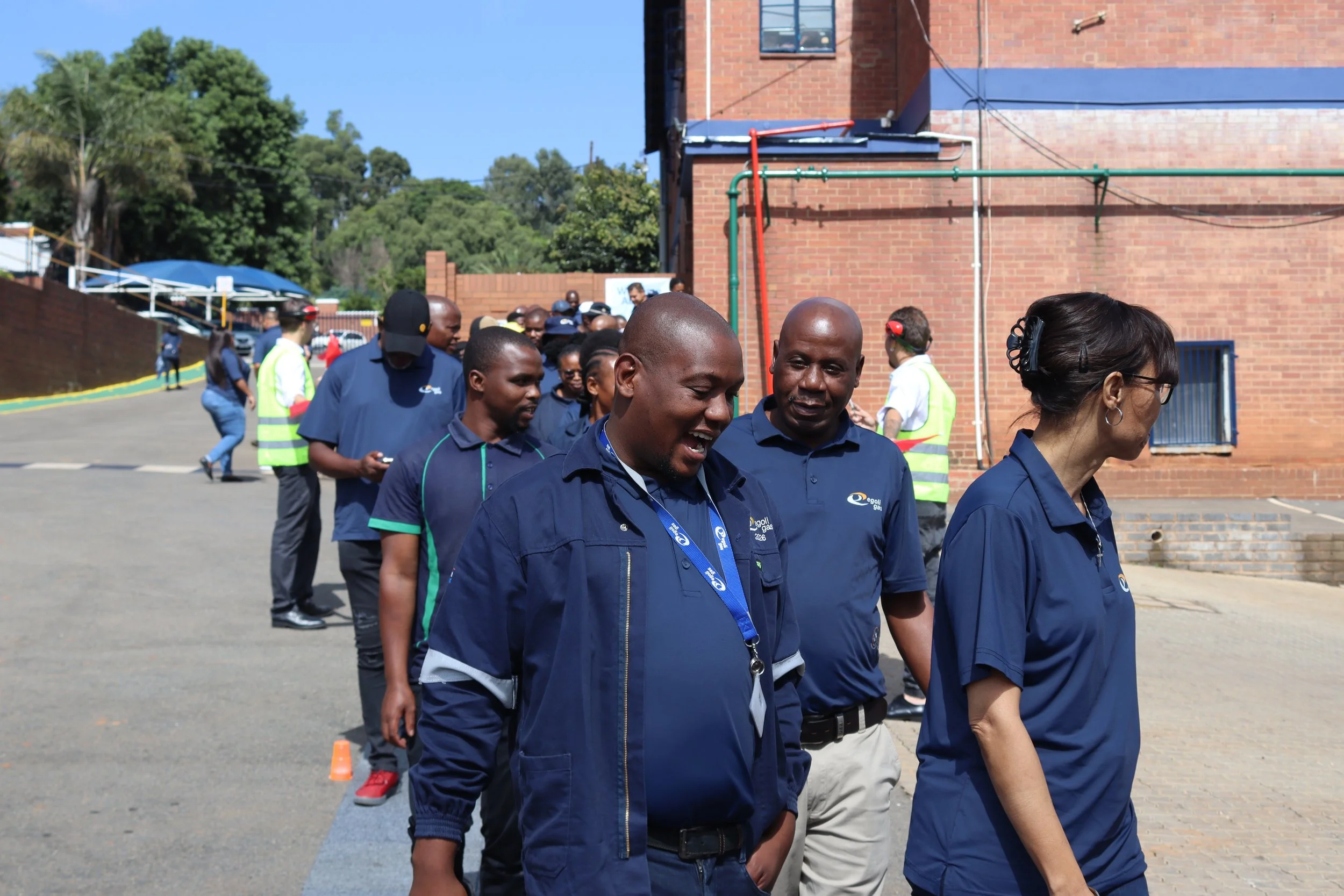 A group of people walking in a line outdoors near a red brick building on a sunny day.