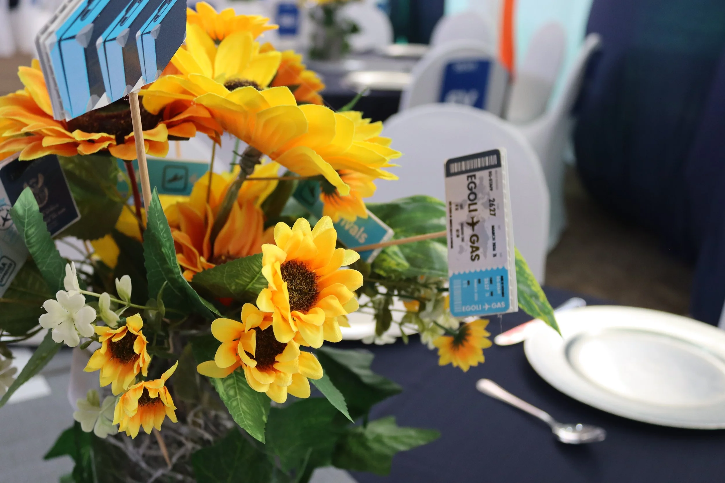 Artificial sunflower flower arrangement with yellow petals and green leaves, placed on a table with price tags attached.