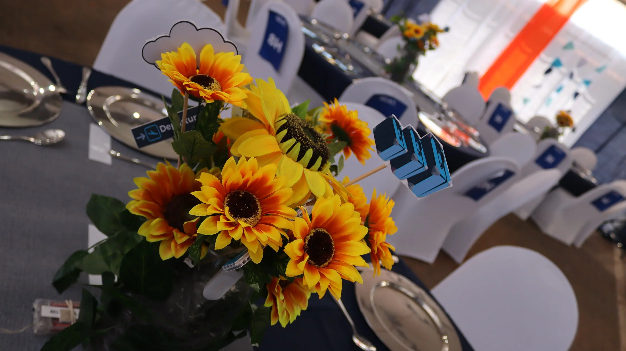 A table decorated with a sunflower centerpiece and set with silverware, plates, and napkins, likely for a formal event or banquet.