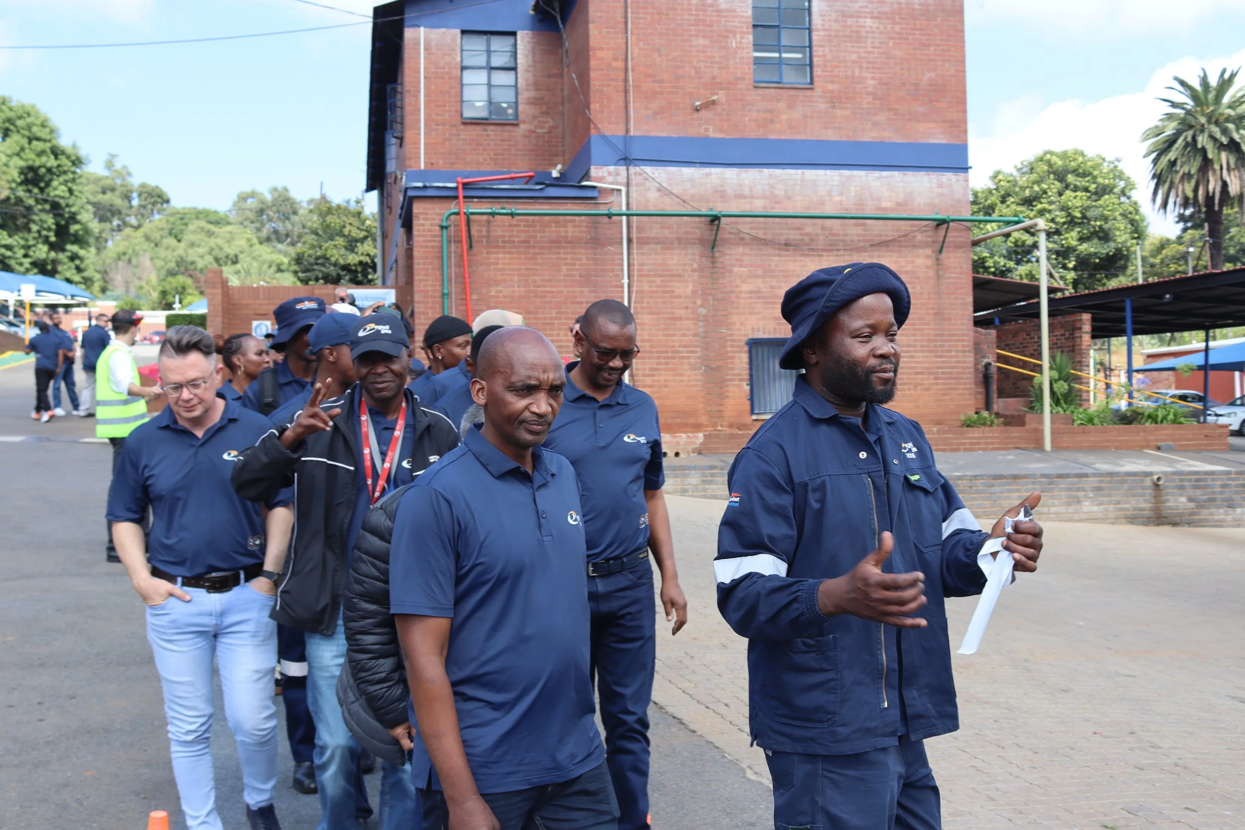 A group of people wearing navy blue shirts walking outdoors in front of a brick building with trees in the background.