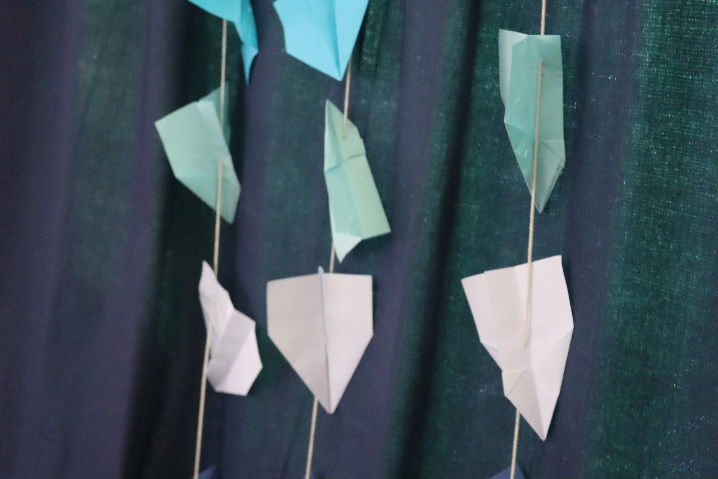 Colorful paper origami hearts hanging on strings against a dark green background.
