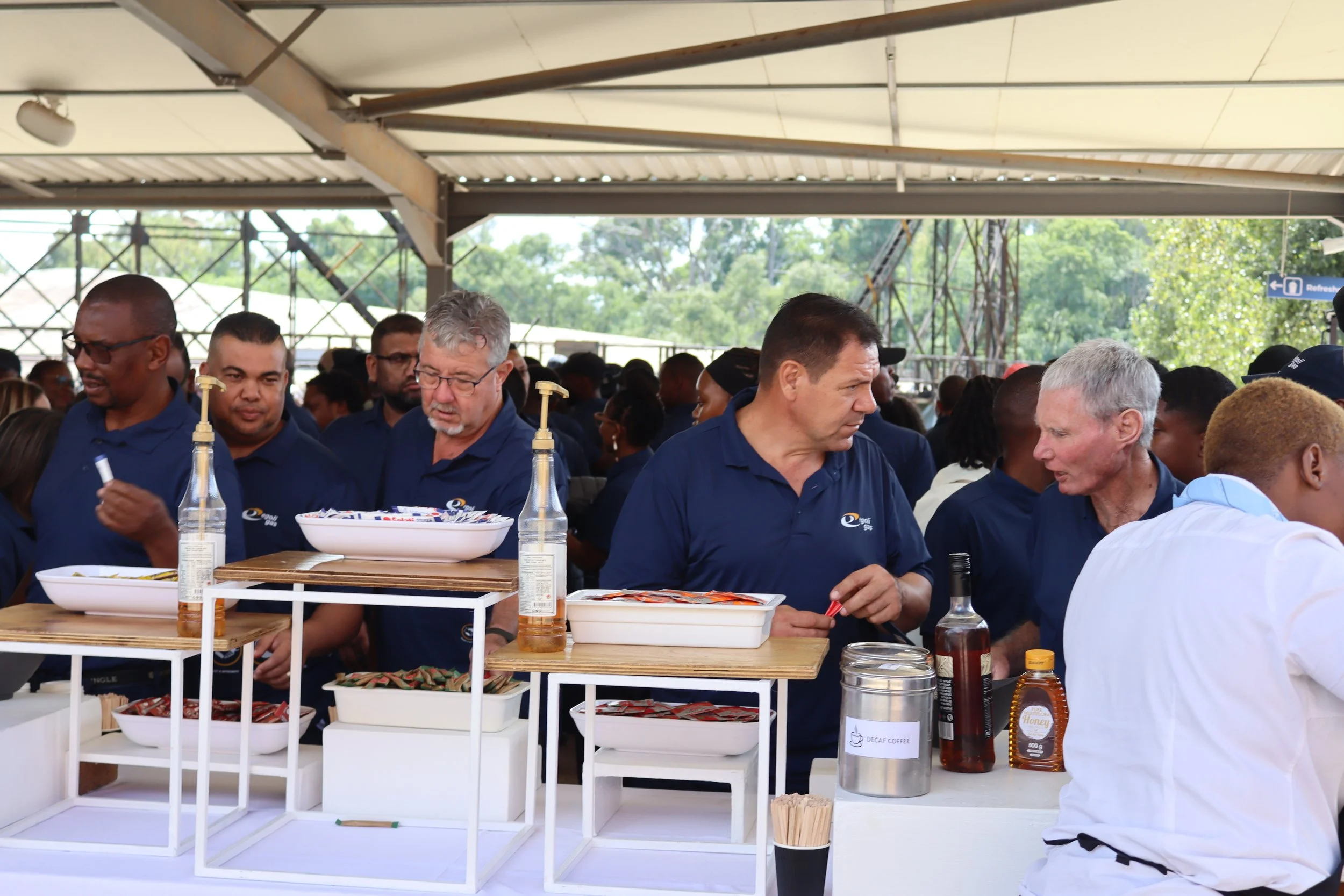 People gathered at a food stand under a tent, serving and enjoying various dishes and drinks.