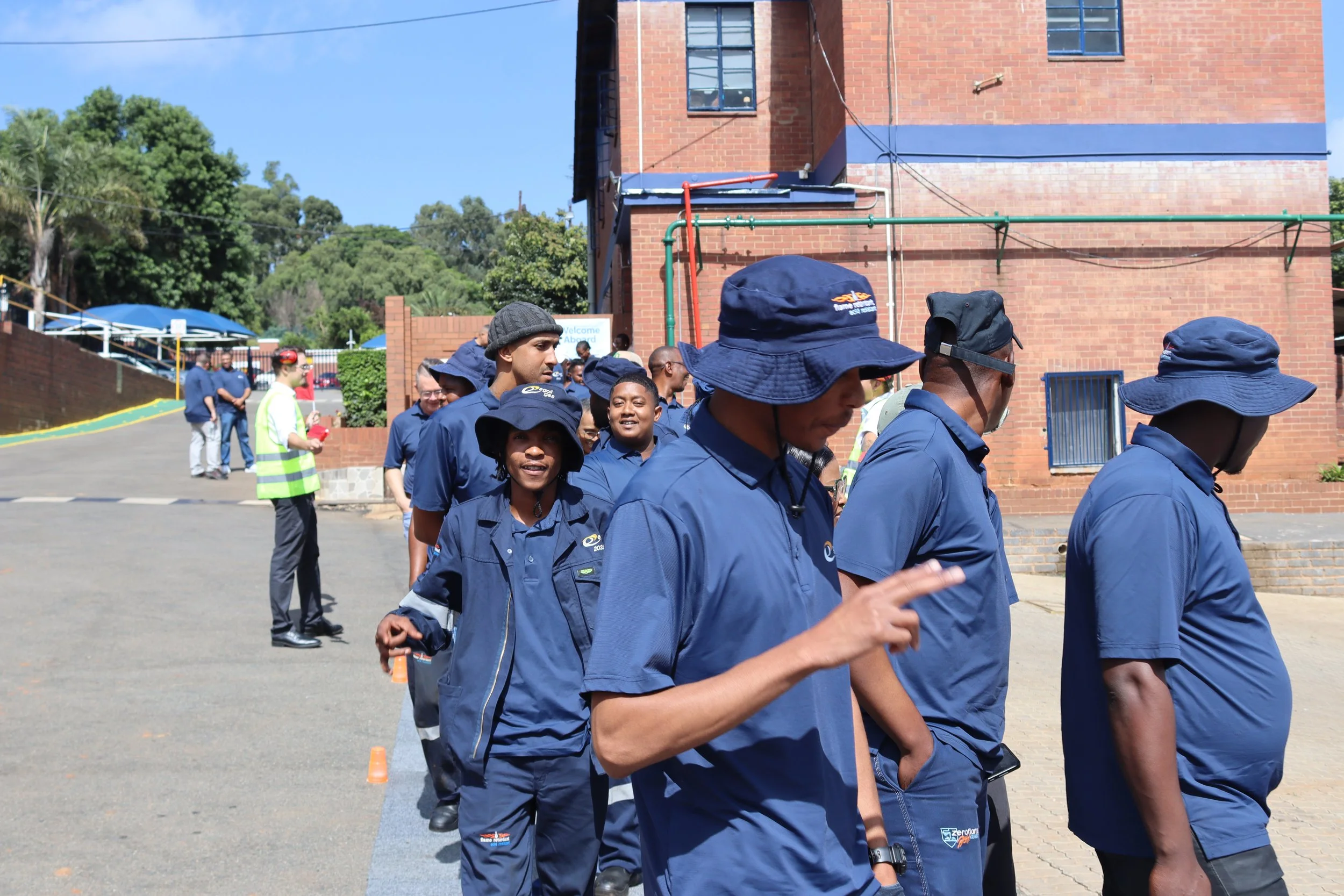 Group of people dressed in navy blue clothing standing outdoors, with some wearing hats, in front of a brick building.