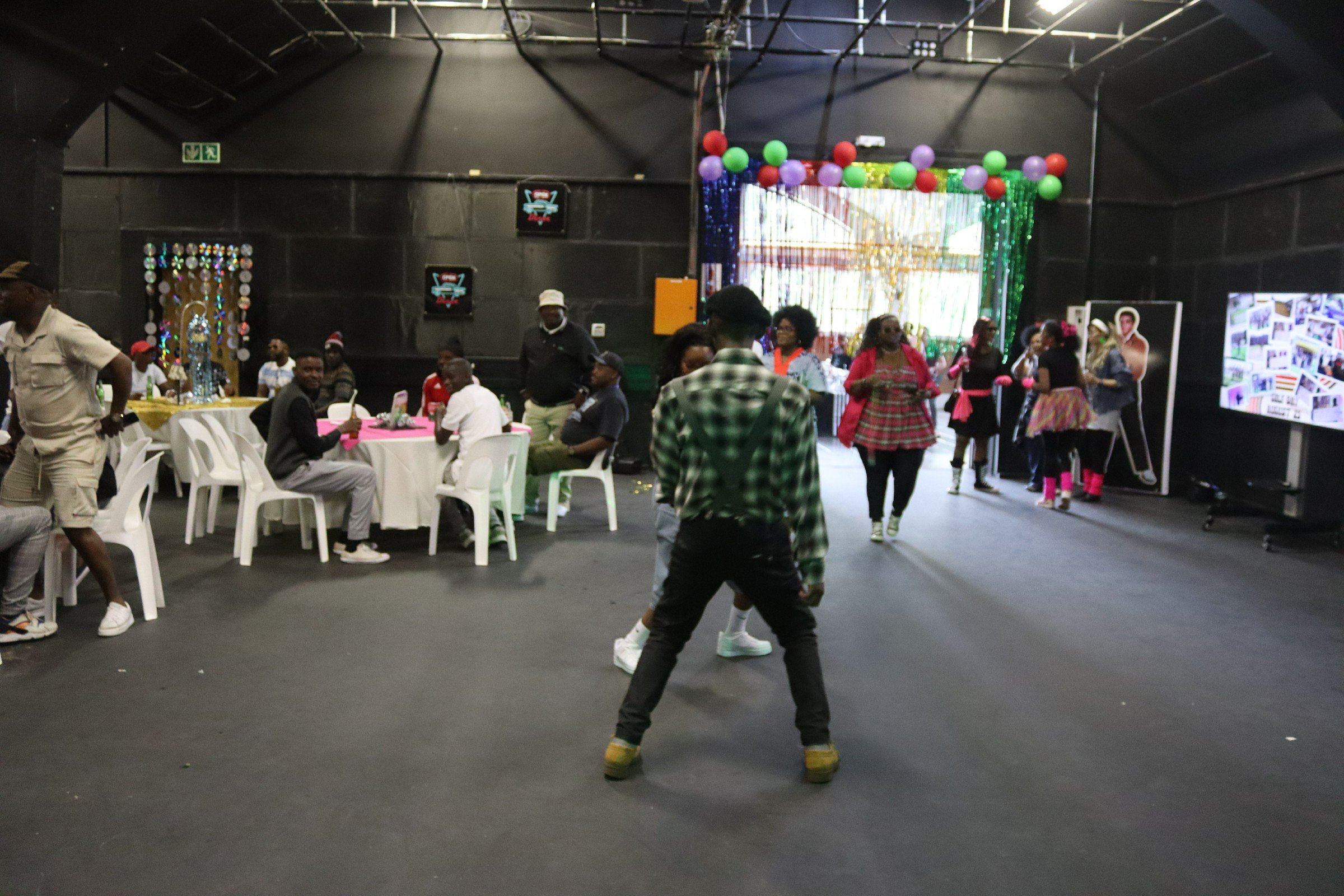 People celebrating at an indoor party with colorful balloons, decorations, and a photo display.