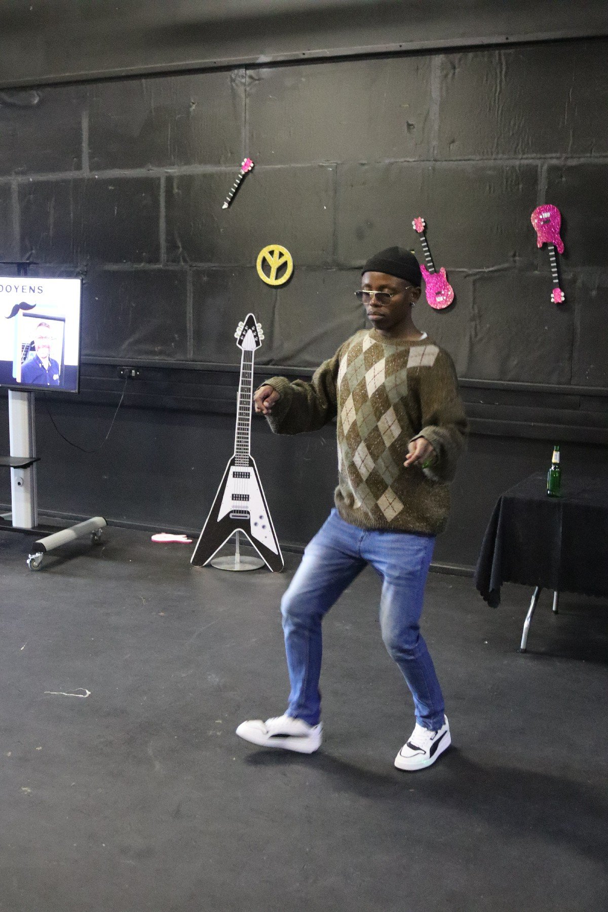 A person dancing in a room decorated with musical-themed decorations, including guitars and a yellow peace sign on the wall.