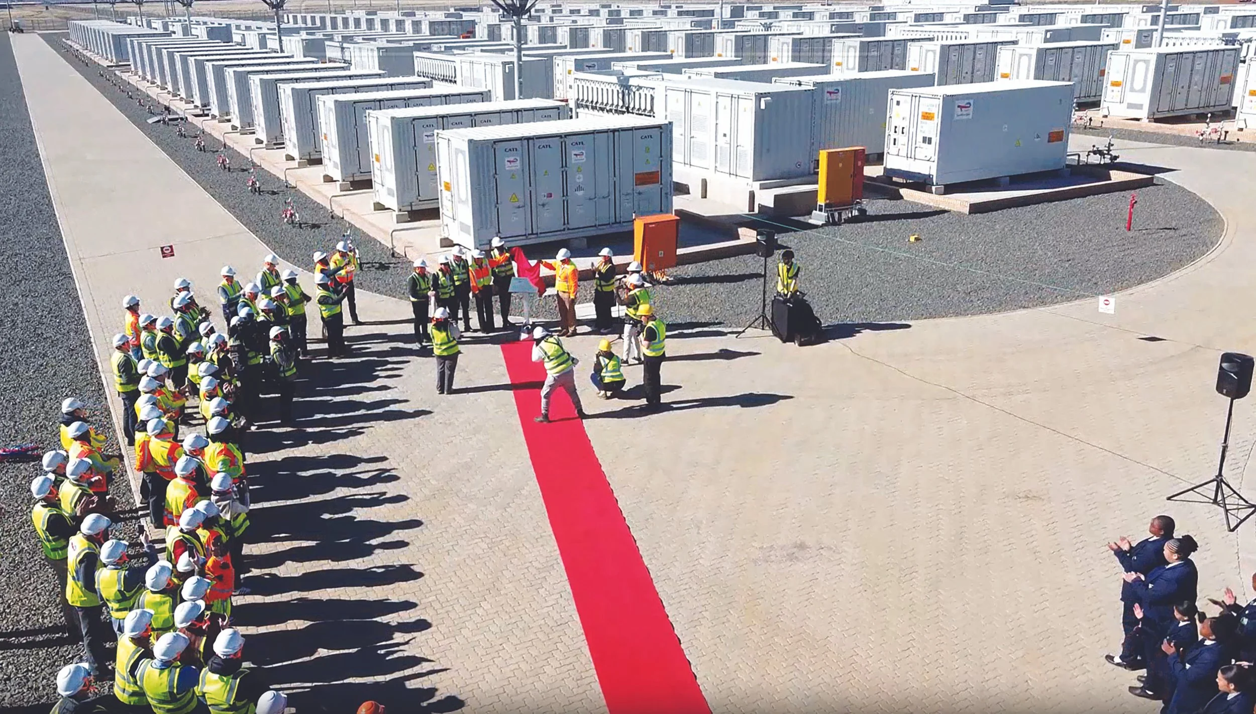 A Group of people in safety vest's with a red carpet and container's in the background.