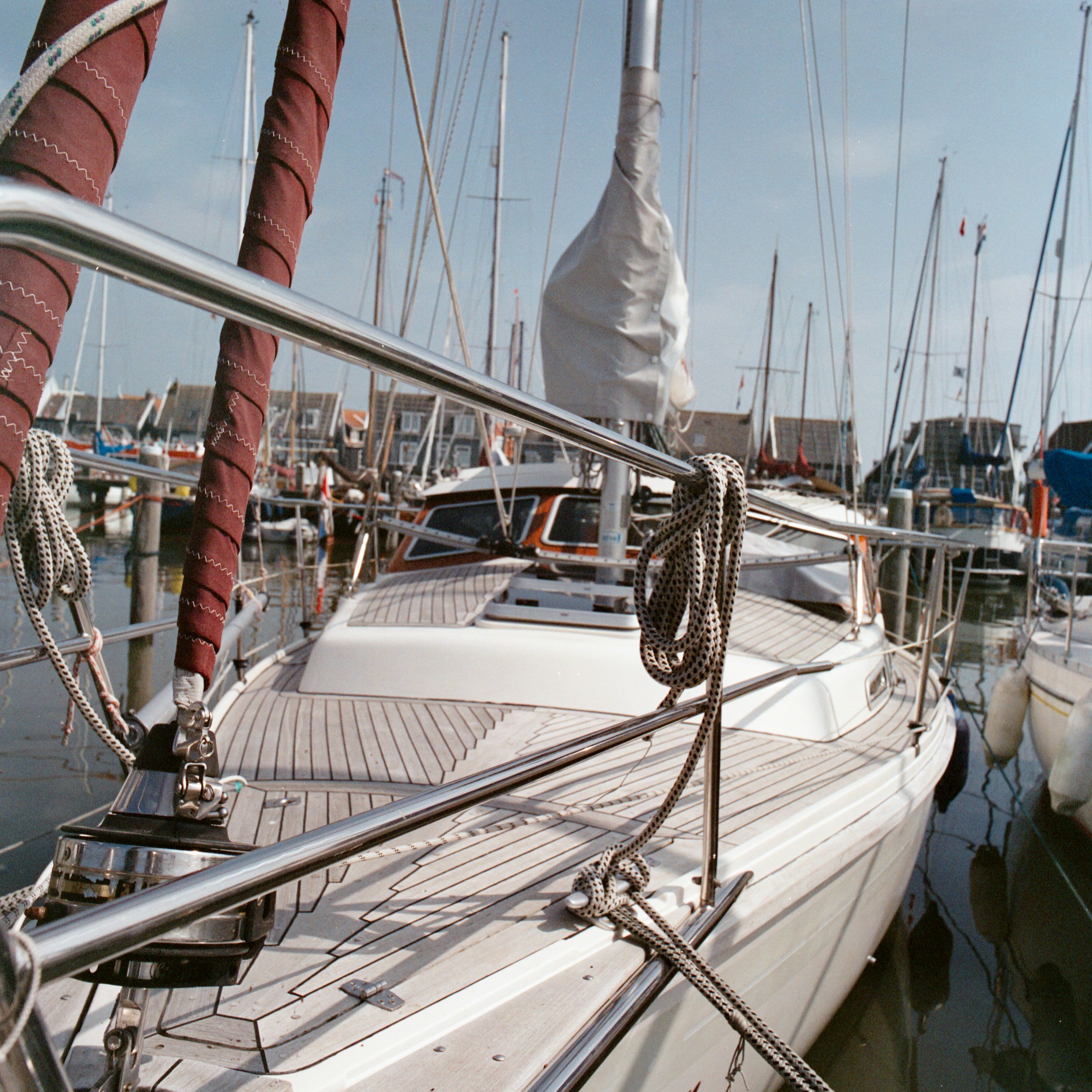 A boat docked at a marina with masts of other boats in the background, ropes, and a wooden deck visible.