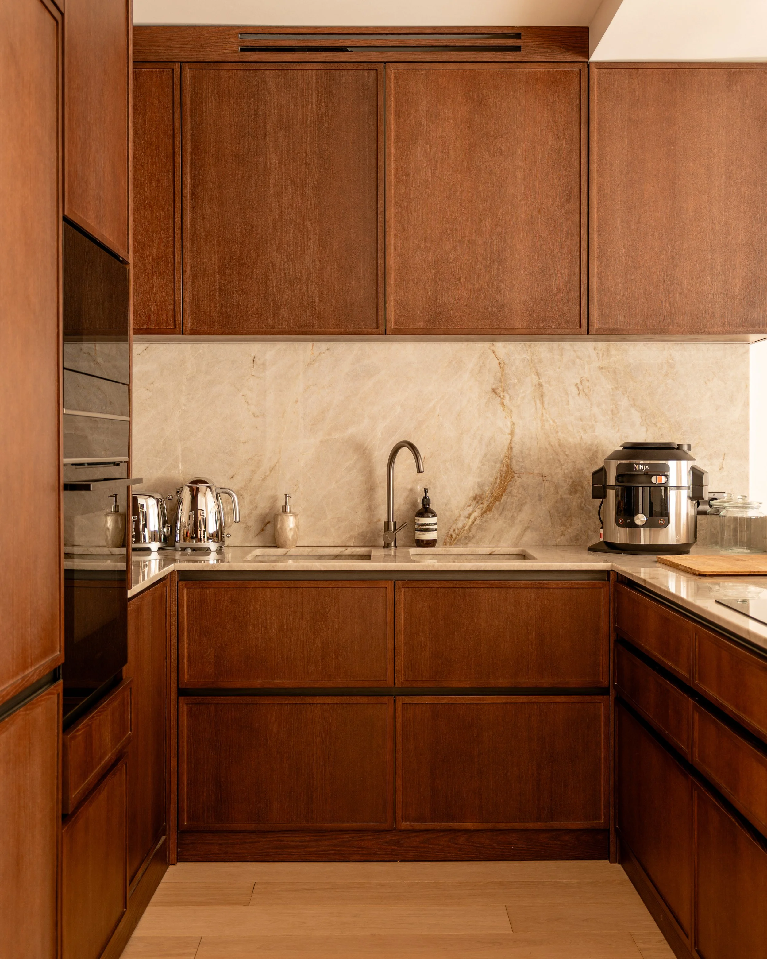Wooden kitchen cabinets with marble backsplash, a stainless steel sink with a curved faucet, and a few small appliances on the countertop.