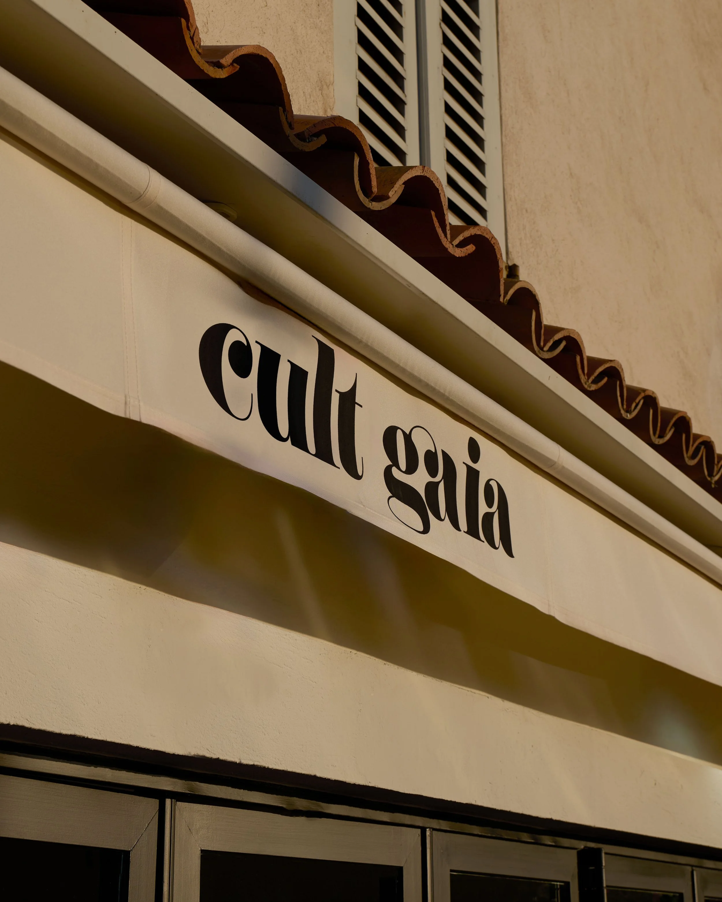 Close-up of a white sign with black text on a beige building wall, part of the shop's signage reading 'salad,' with a mailbox or vent above it and window shutters in the background.