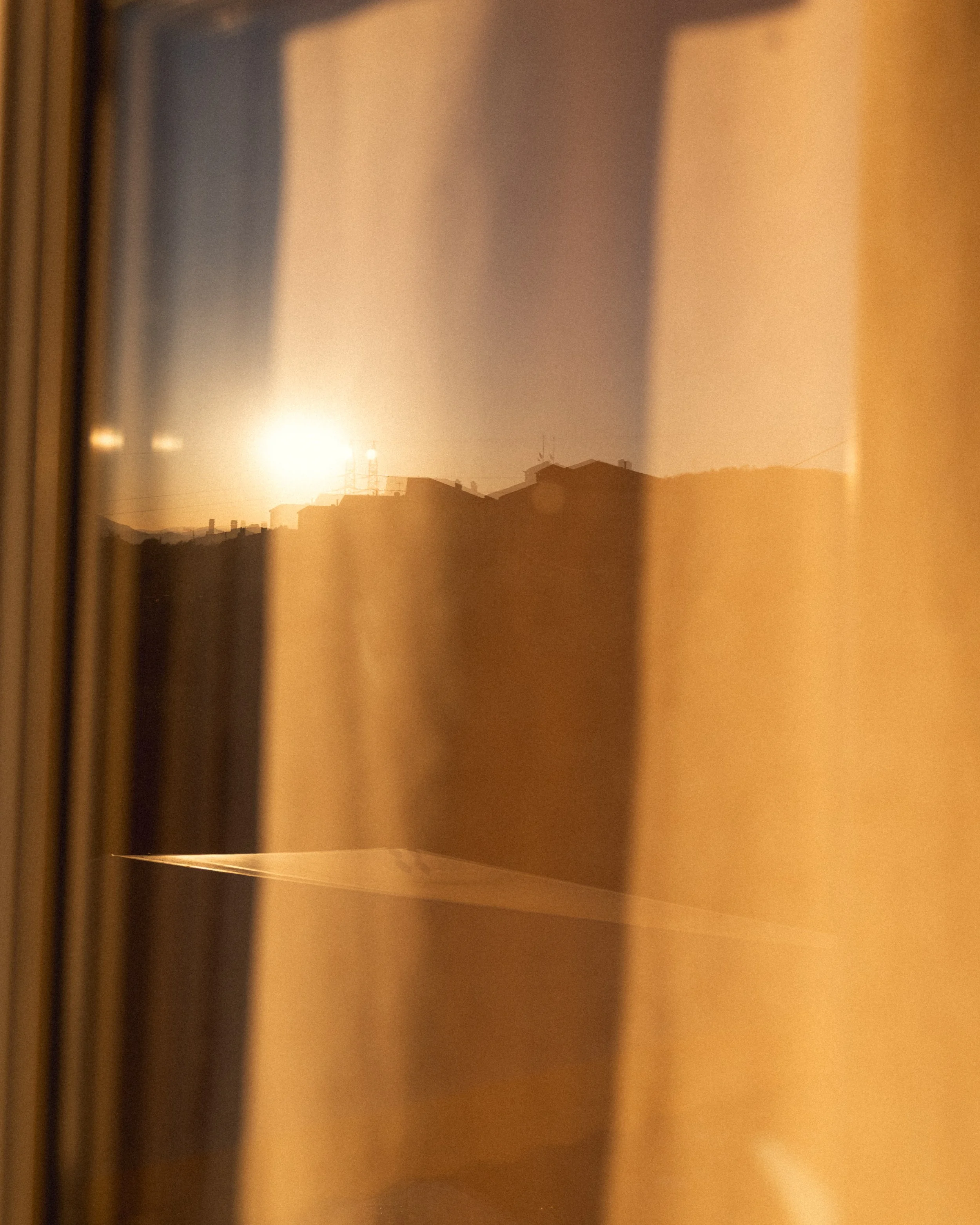 A blurry, warm-colored landscape seen through a narrow window or curtain.