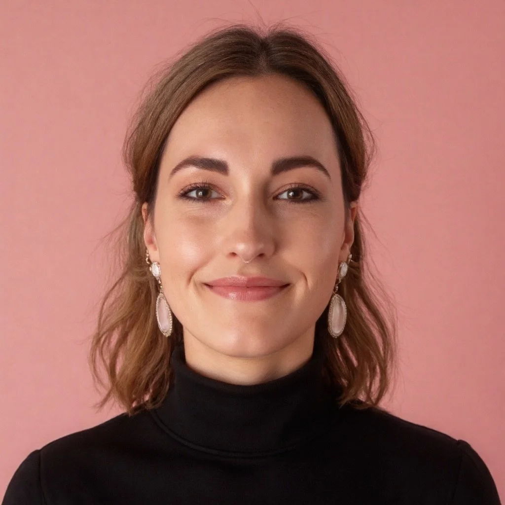 Close-up portrait of a woman with shoulder-length brown hair, wearing earrings and a black turtleneck, smiling slightly against a pink background.
