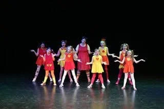 Group of young girls in colorful costumes performing a dance on stage.