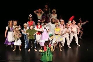 Children and adults dressed in colorful costumes performing a dance on stage.