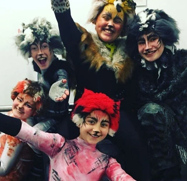 Group of children dressed in cat costumes and face paint, smiling and posing for a photo.