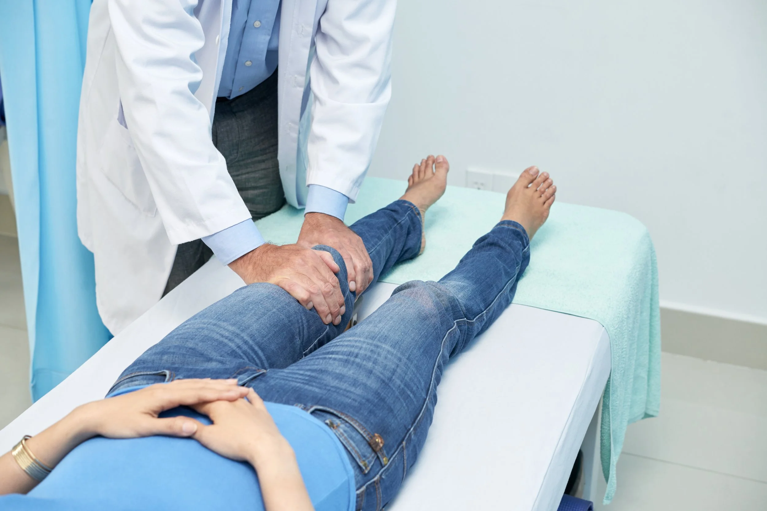 Doctor performing a physical examination on a patient's legs in a medical room.