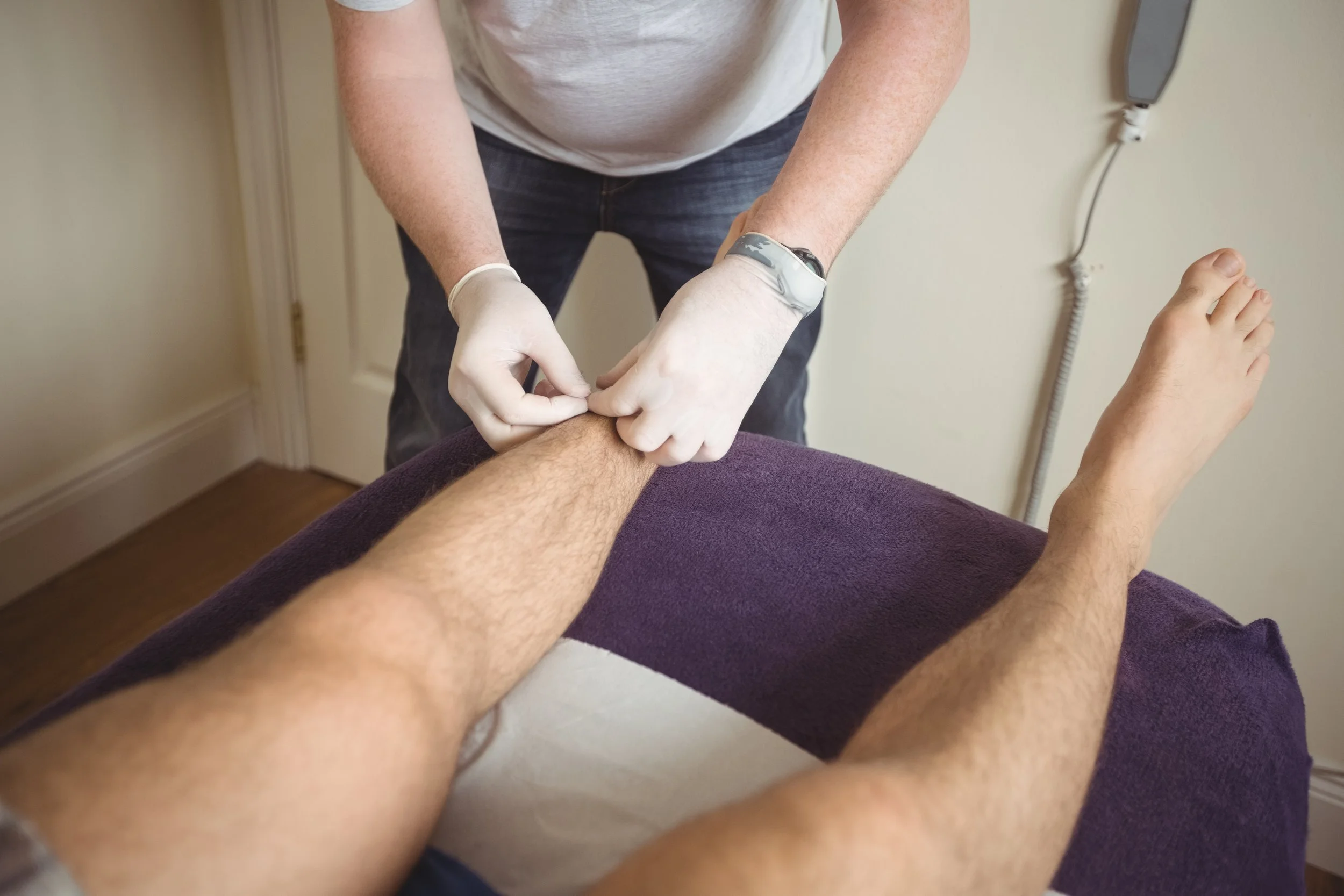 Medical professional wearing gloves checking a patient's leg during a healthcare procedure.