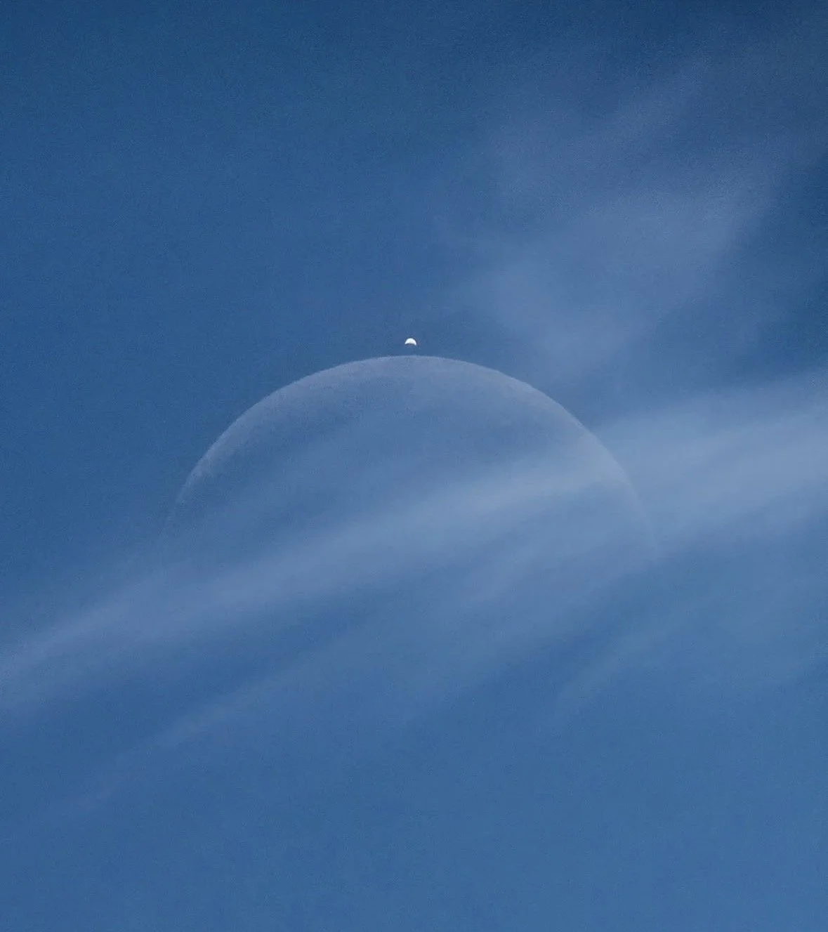 De maan die door een dunne laag bewolking schijnt, zichtbaar boven de horizon tegen een blauwe hemel.