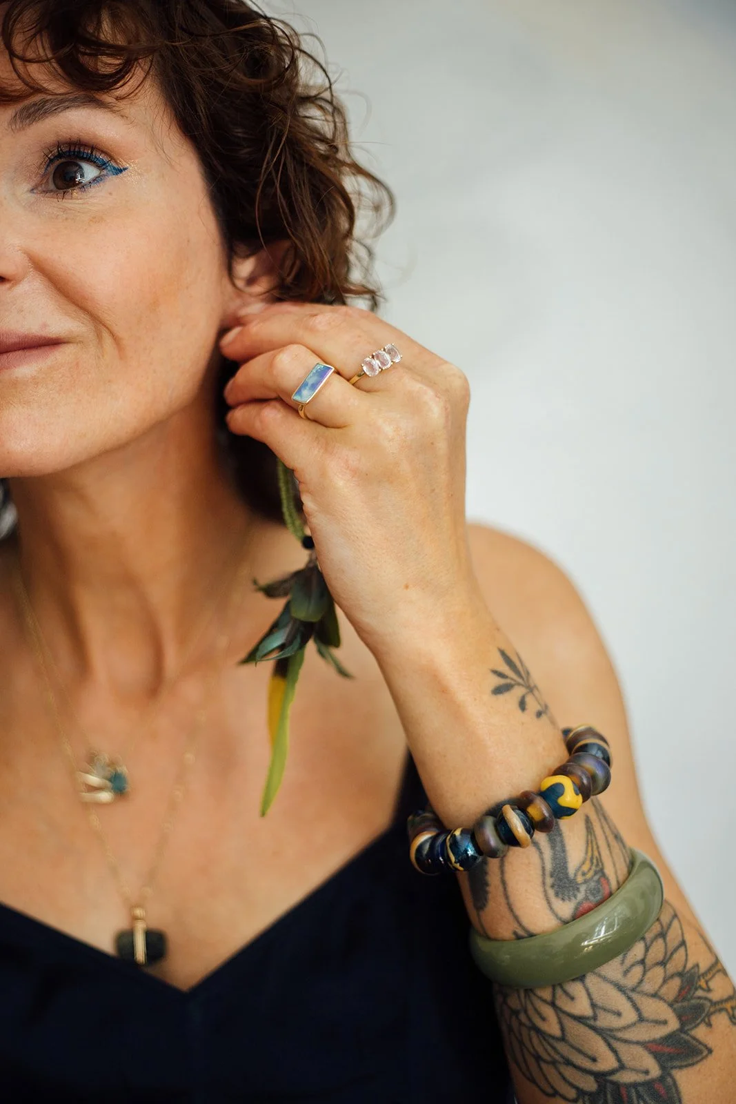 Close-up van een vrouw met sieraden en tatoeages, die haar hand bij haar oor houdt.