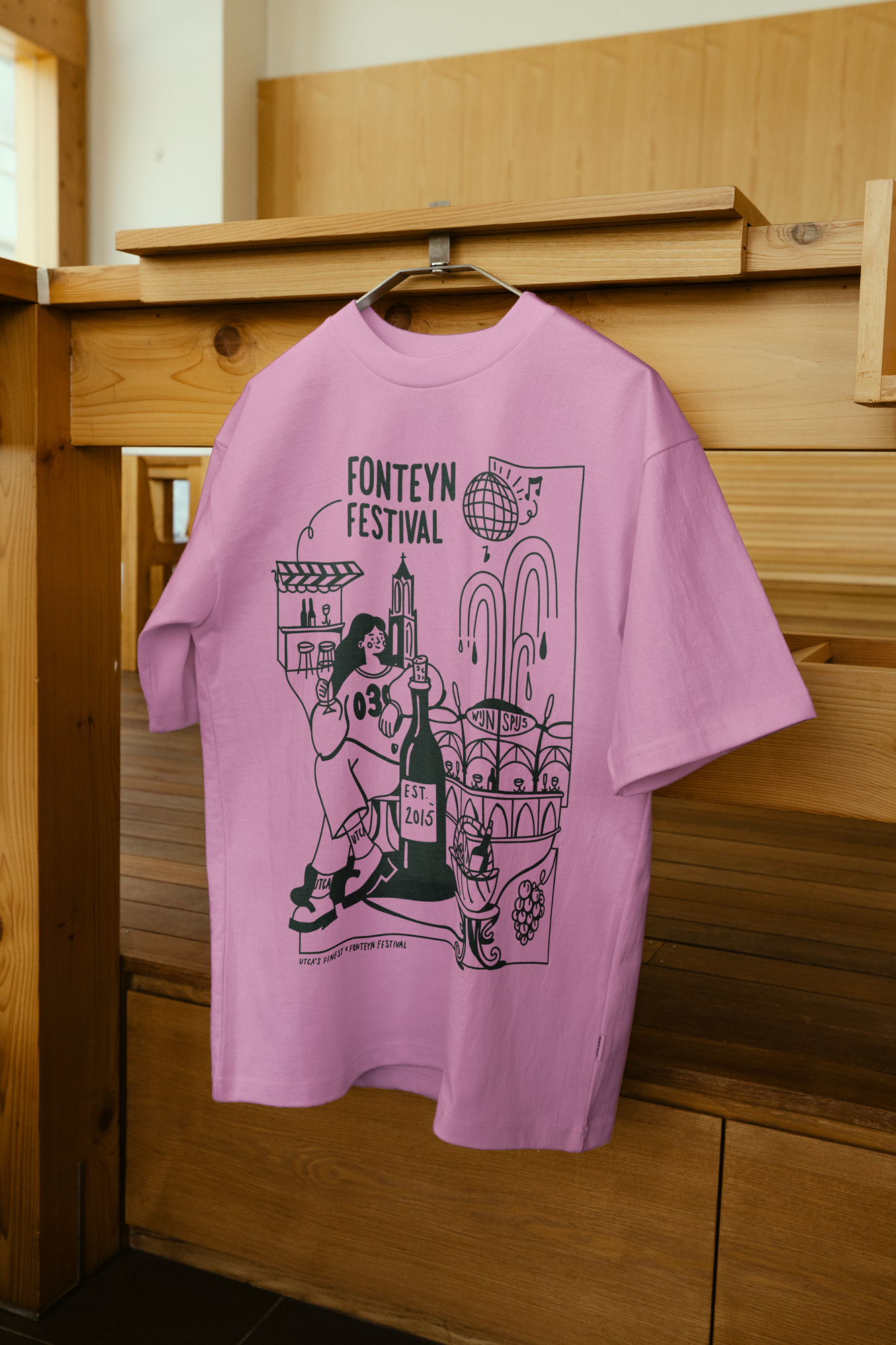 Fonteyn Festival Utrecht shirt design door Temple Isle Trademark. Roze T-shirt met tekst en illustraties die verwijzen naar een festival, hangt aan een kledinghanger.