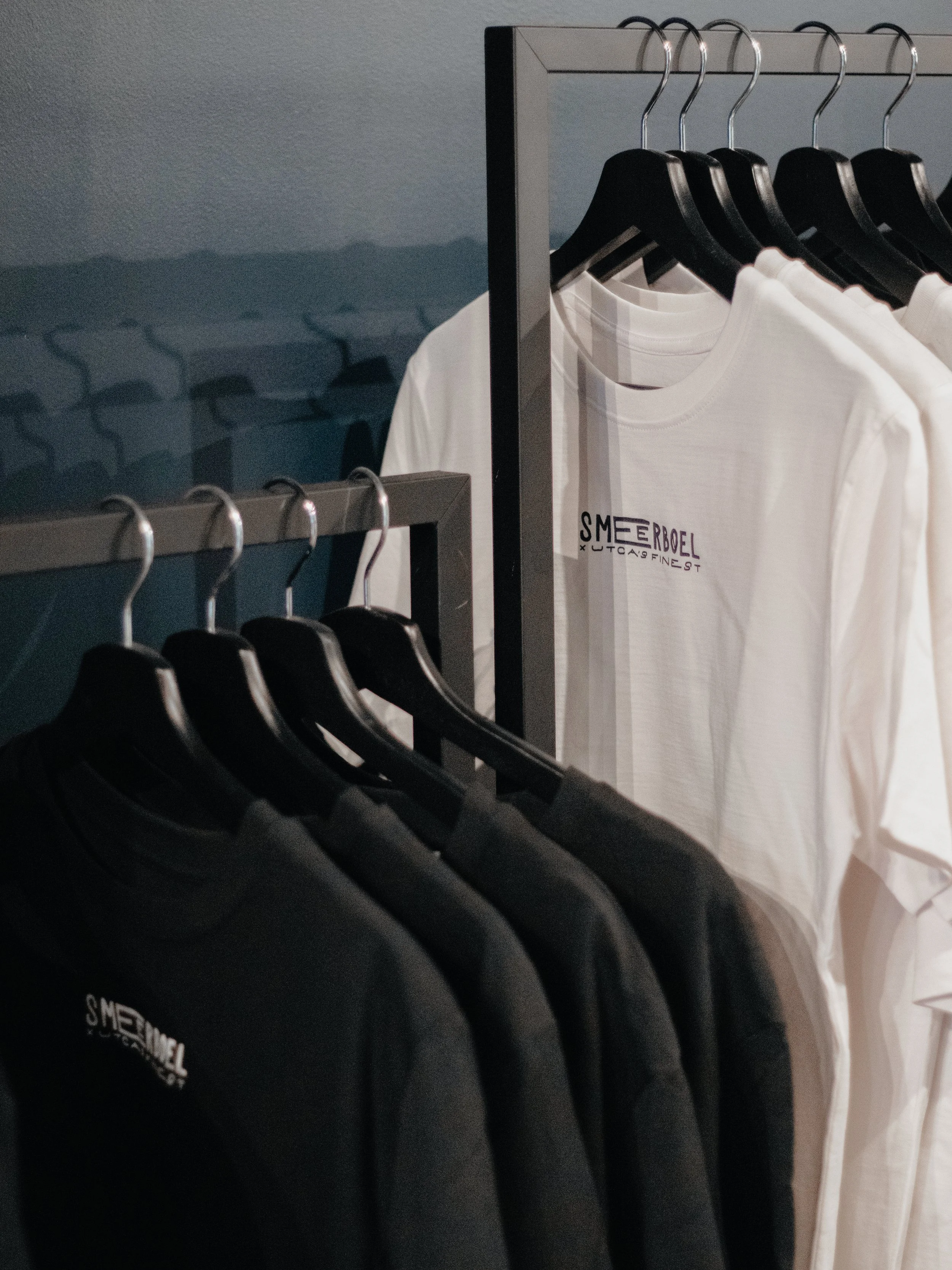 Rij t-shirts en hoodies op een kledingrek, de meeste zijn zwart en sommige zijn wit.