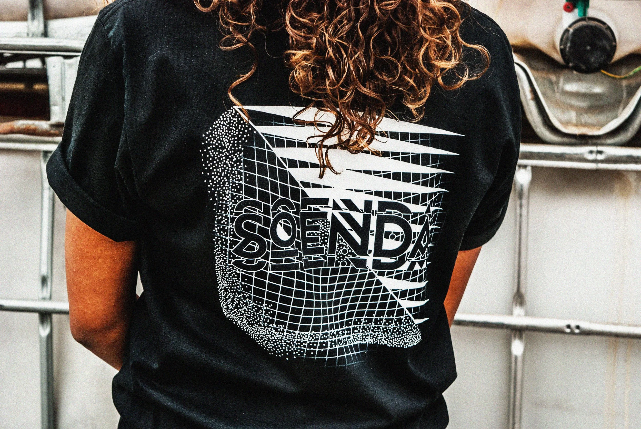 Persoon met lang, kroezend haar draagt een zwart T-shirt met een grafisch witte ontwerp en tekst.