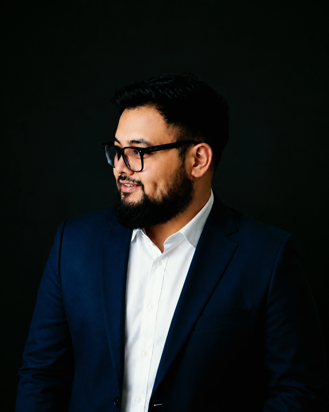 Professional man with glasses and beard in a dark suit against black background