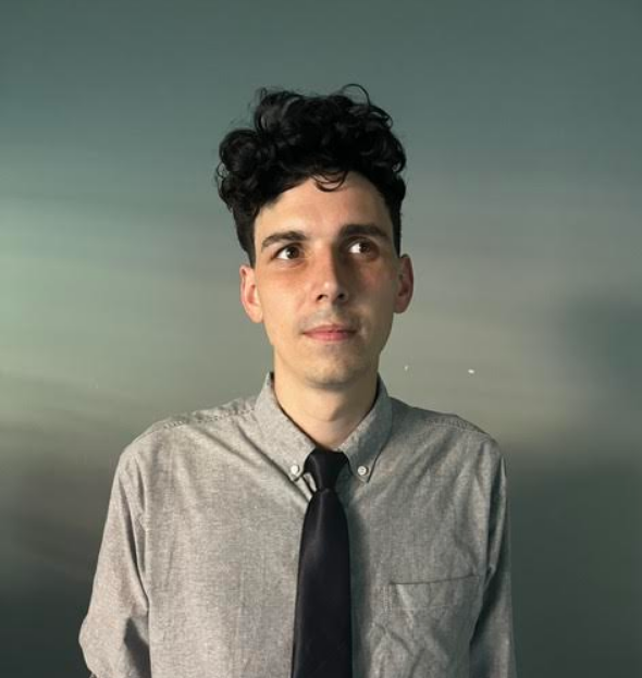 A young man with black curly hair, wearing a light gray button-up shirt and a black tie, looking off to the side against a gradient background.