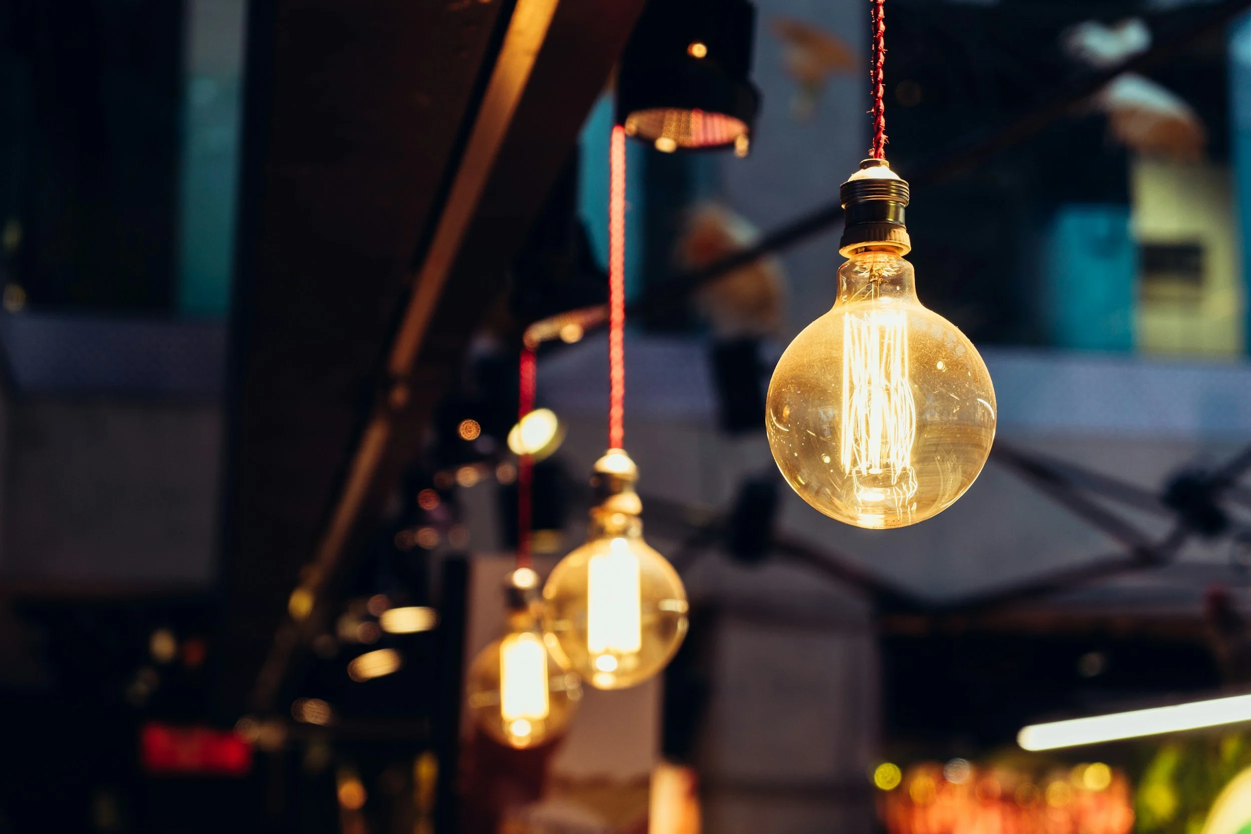 Close-up of vintage filament light bulbs hanging from cords, glowing warmly in a dim setting.