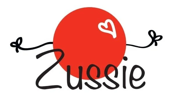 Cartoon illustration of a red ball with a small white heart on it, and the words "Zussie" written underneath in black playful font.