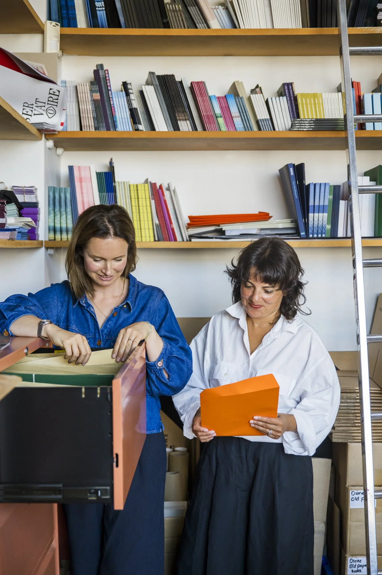 Founders going through papers in a file cabinet with colourful books on shelves next to a ladder