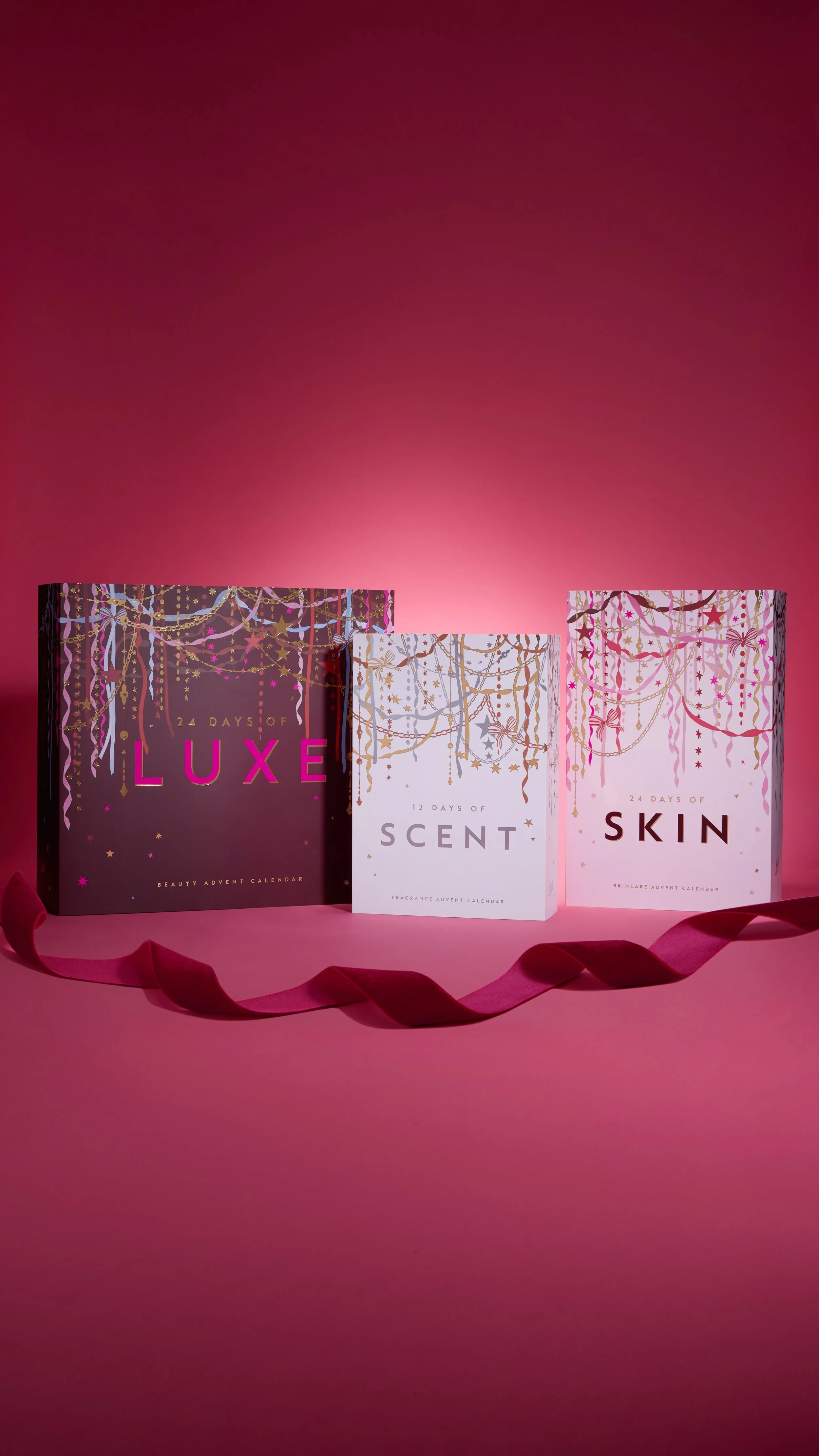 Three premium advent calendars: 24 Days of Luxe beauty in purple and gold packaging, 12 Days of Scent fragrance in white and gold packaging and 24 Days of Skin skincare in pink and gold packaging. Against a pink background with a red ribbon.