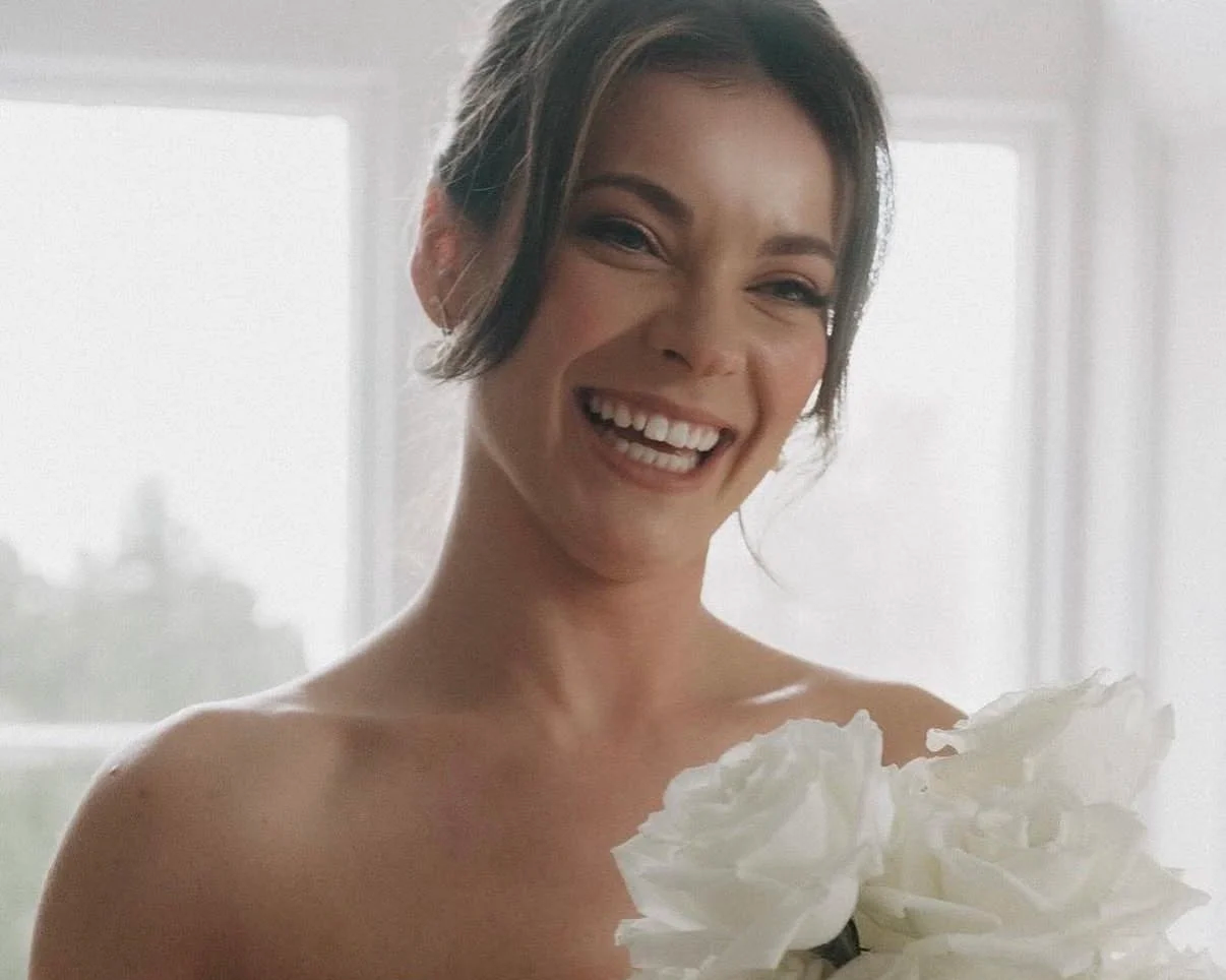 A woman with short brown hair smiling and holding a bouquet of white flowers.