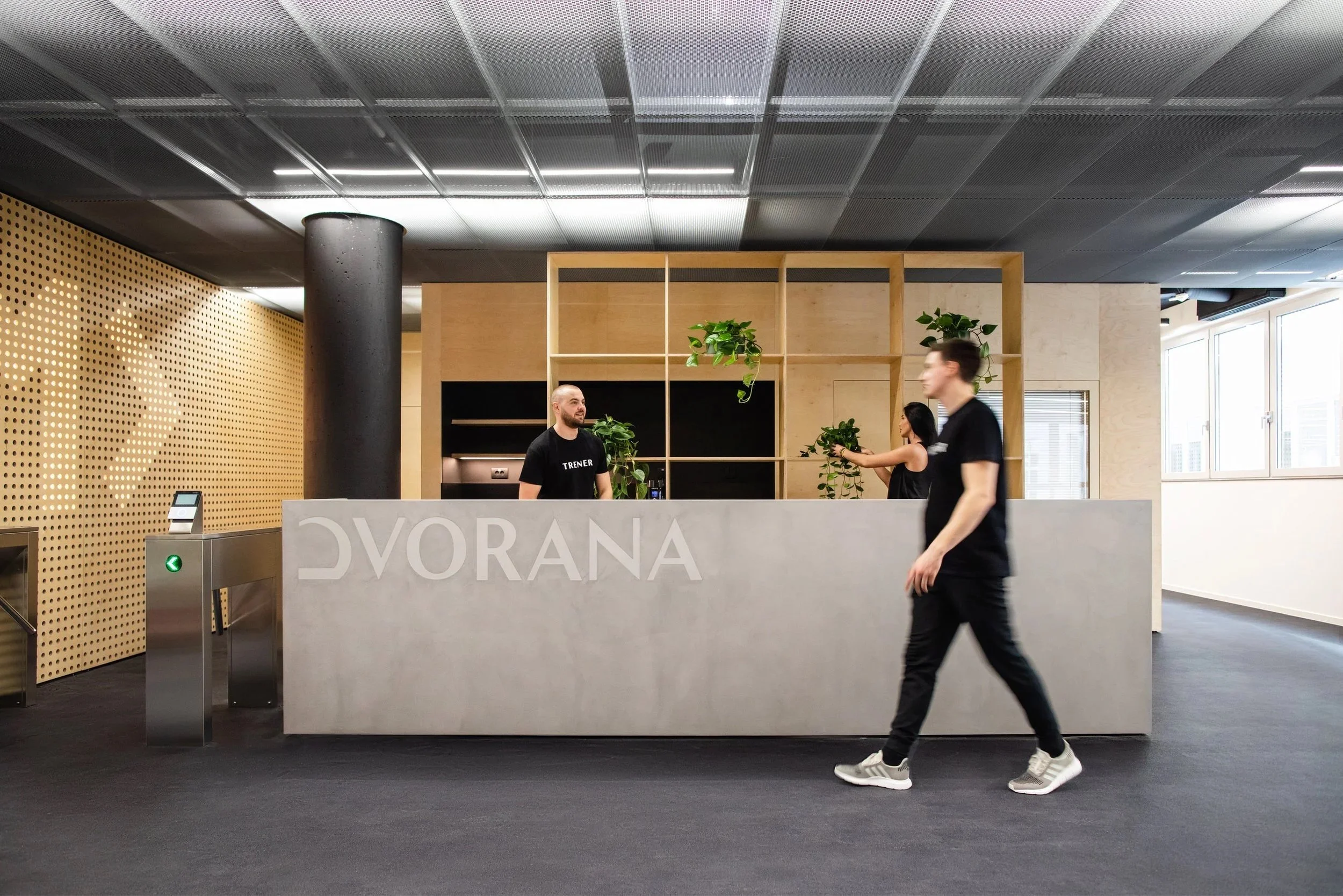 Reception desk with a sign that reads 'DVARANA' in a modern office lobby, with plants and three people; two behind the desk, one walking past.