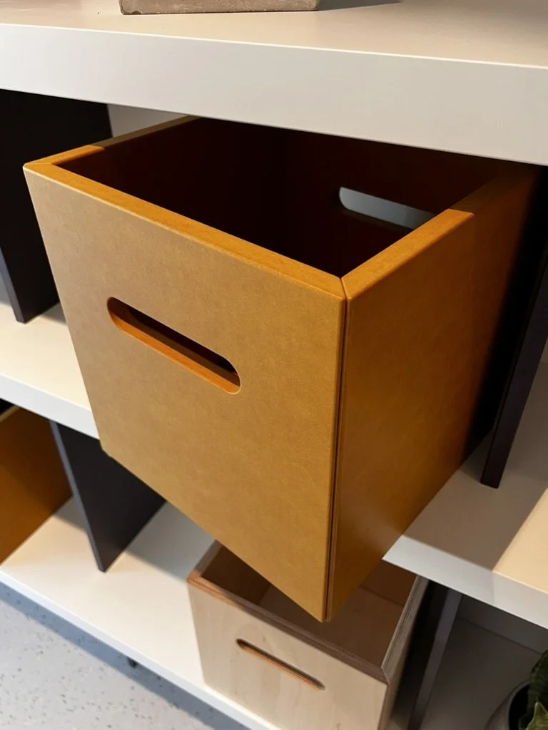 Open orange wooden storage box on white shelf with additional black and white storage boxes around it.