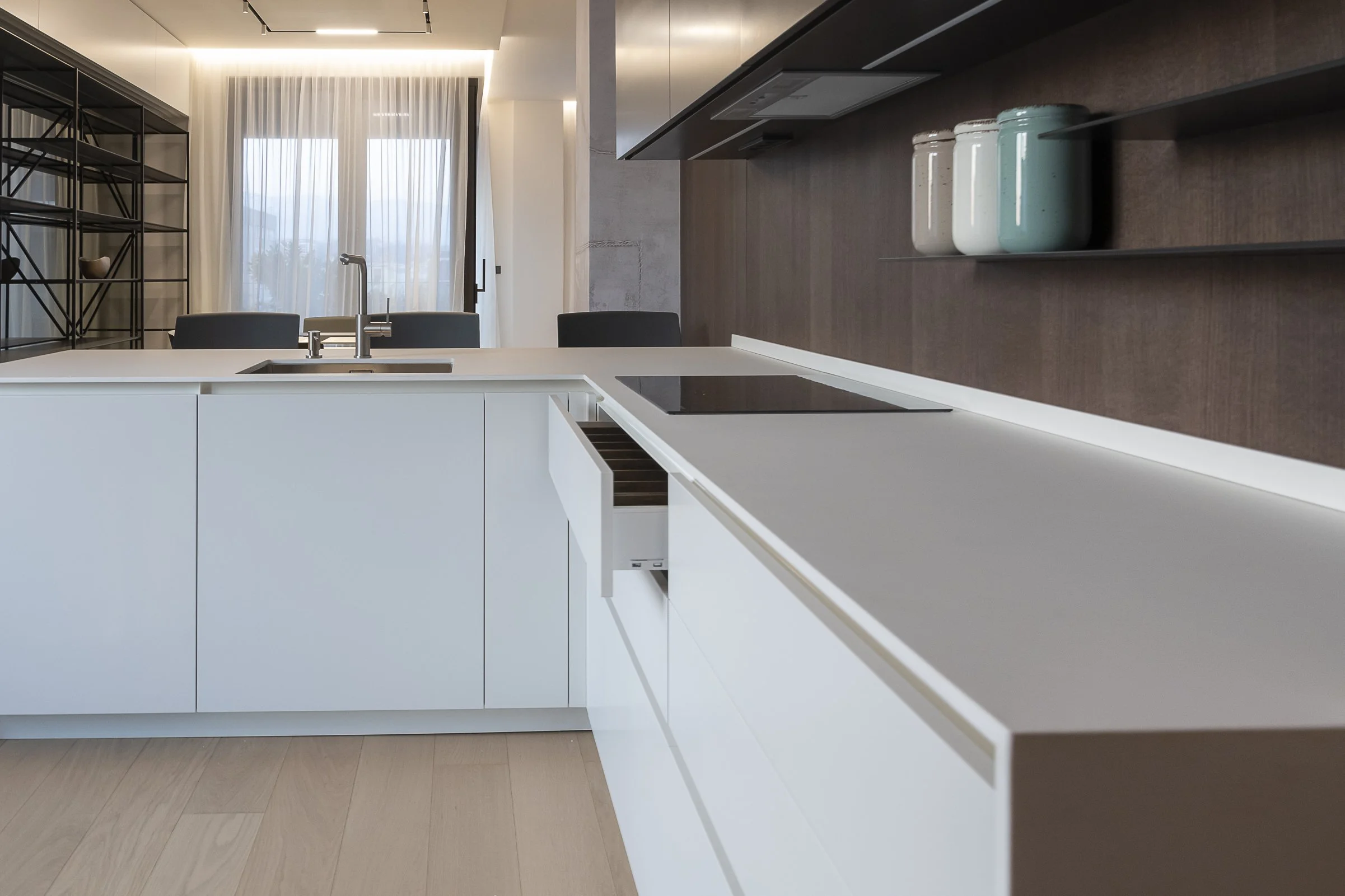Modern kitchen with white island, wooden countertop, black shelving, and large window with sheer curtains.