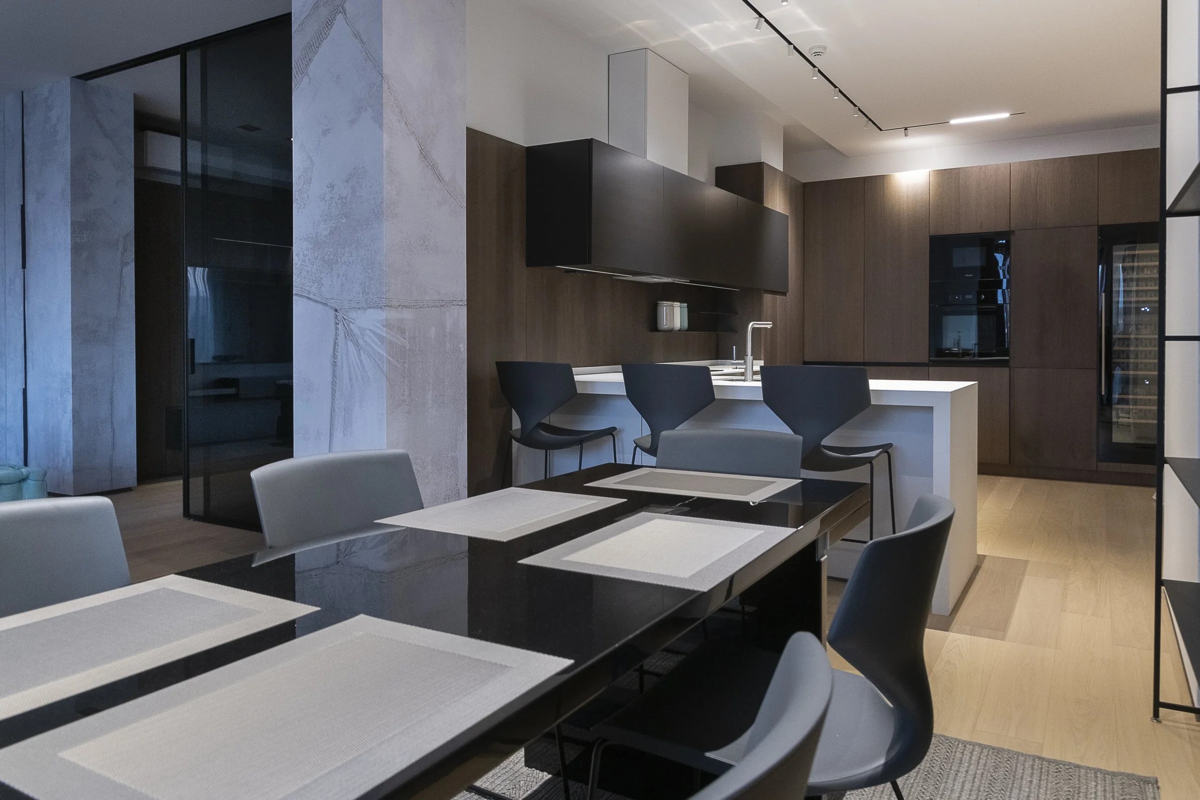 Modern kitchen and dining area with white tabletop, black chairs, wooden cabinets, and a marble backsplash in a sleek, contemporary style.