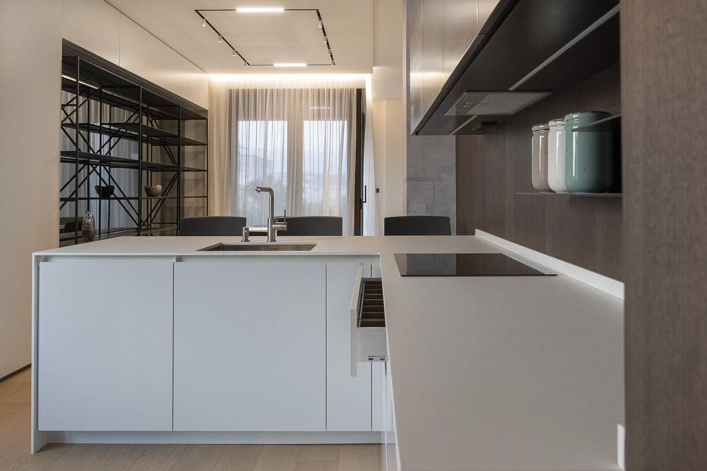 Modern kitchen with white island, black metal shelving, and a large window with sheer curtains.