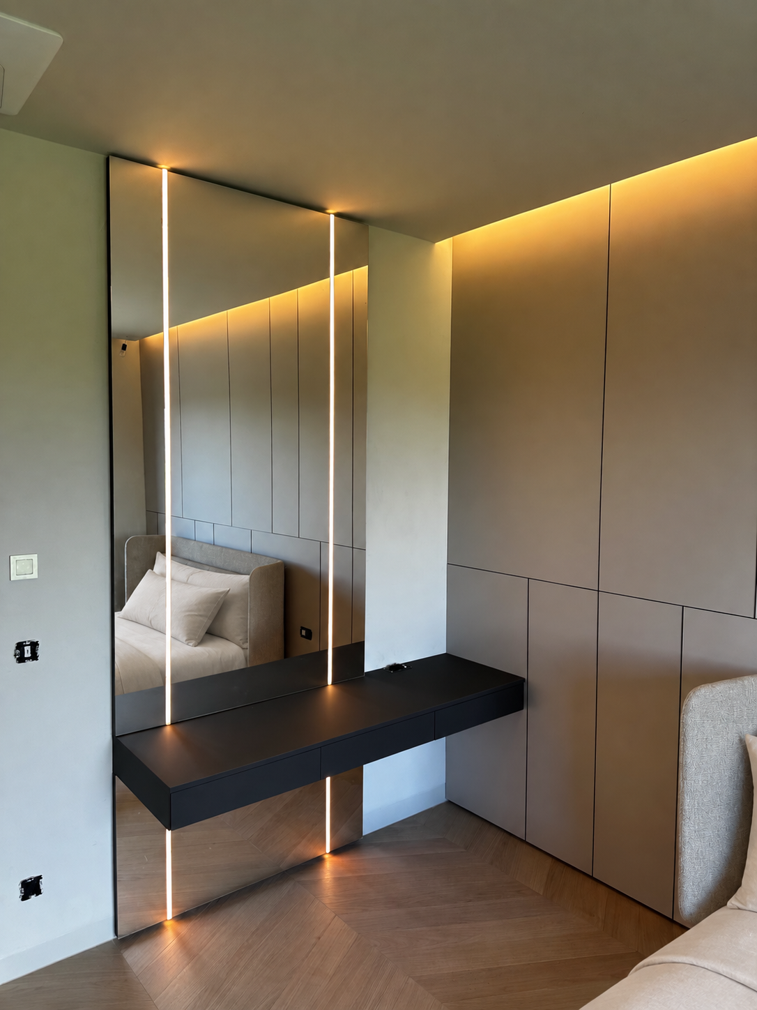 Modern bedroom with beige bed, mirror with LED lights, black floating shelf, wood floor, and minimalist decor.