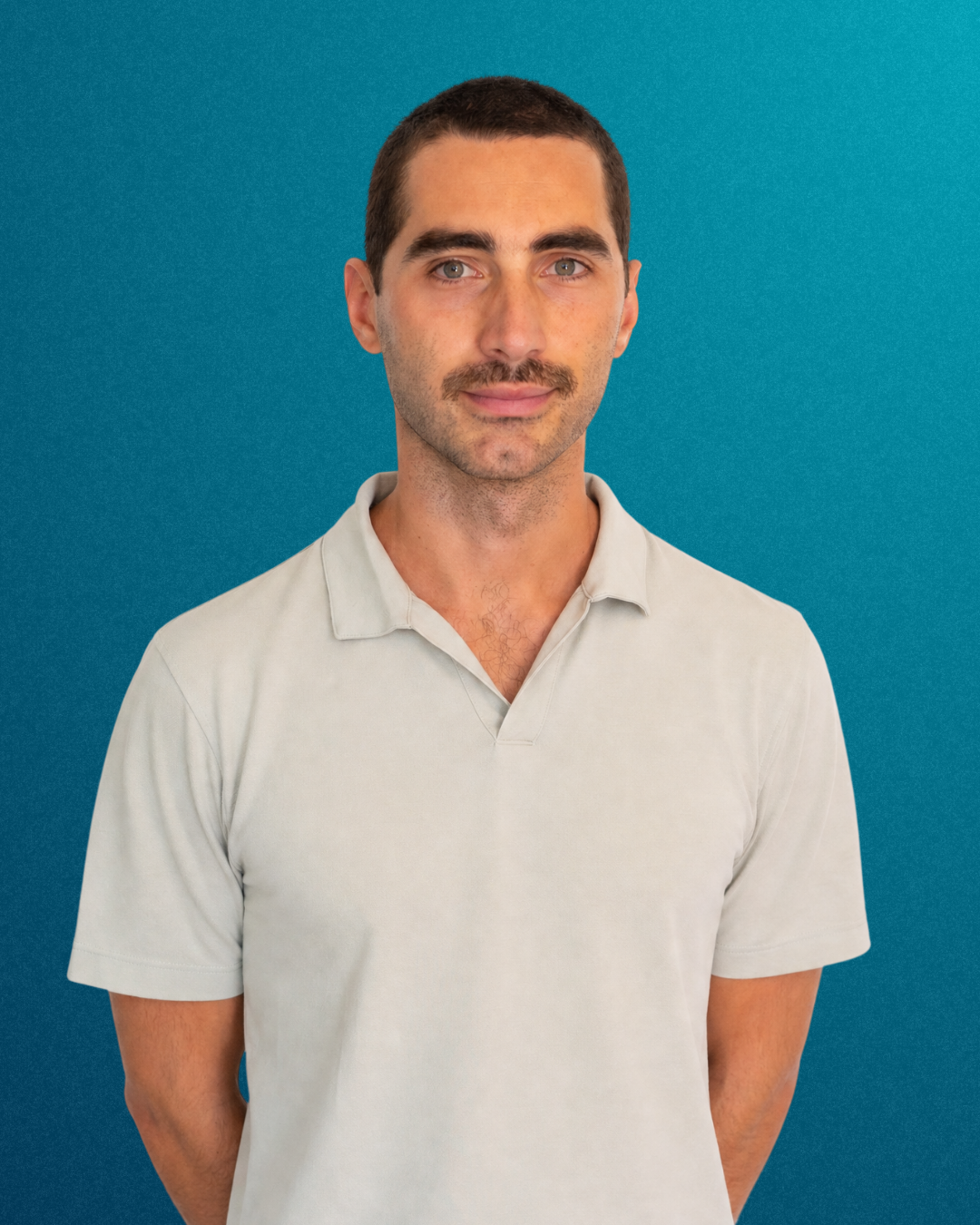 Retrato de un hombre con barba y bigote, con camiseta color crema, de cabello corto, en un fondo azul.
