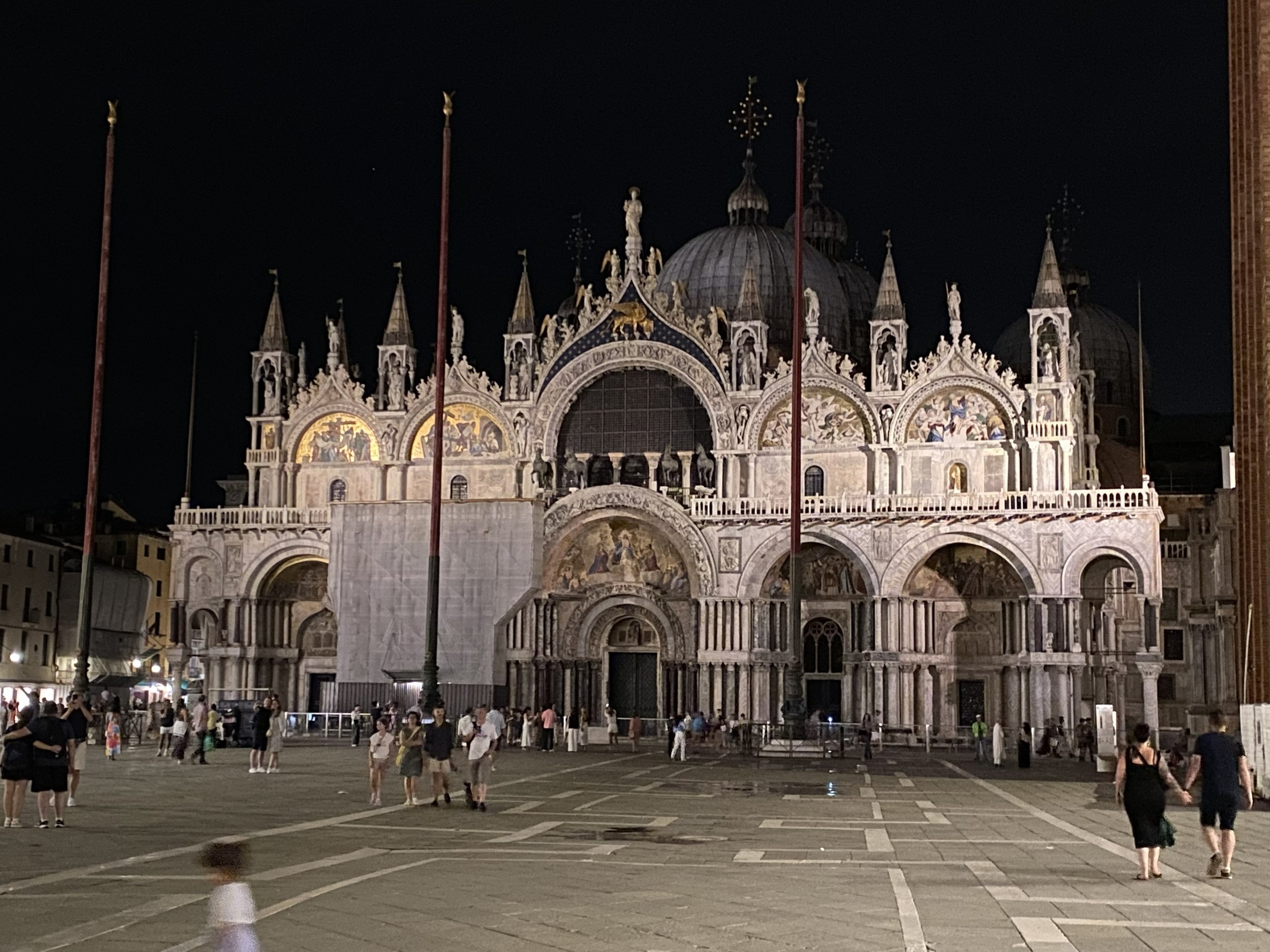 Nighttime view of St. Mark's Basilica in Venice, Italy, with people walking in the square.