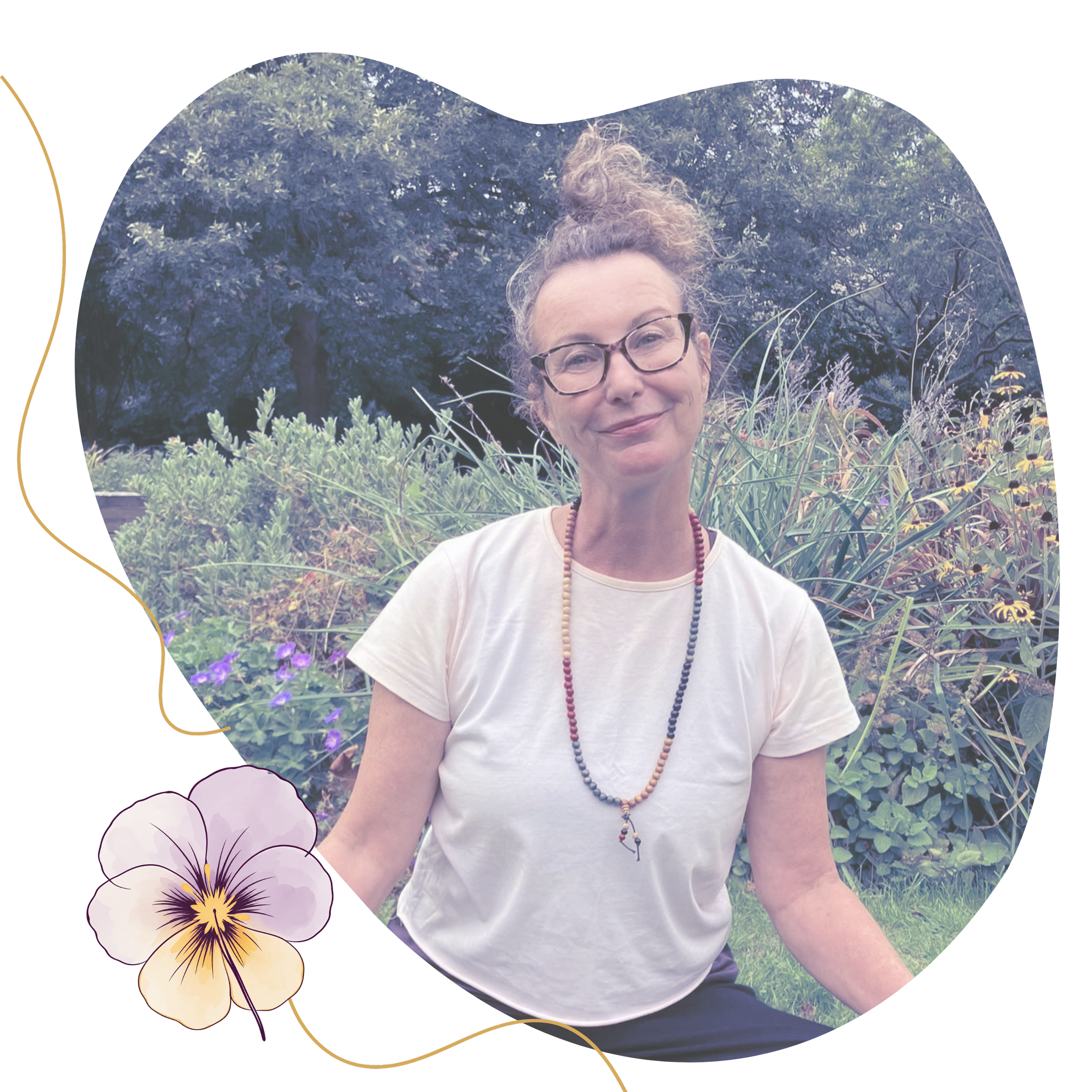 Jane of Heartsease with curly hair and glasses smiling outdoors, surrounded by green plants, trees, and purple flowers doing a yoga class in weston-super-mare