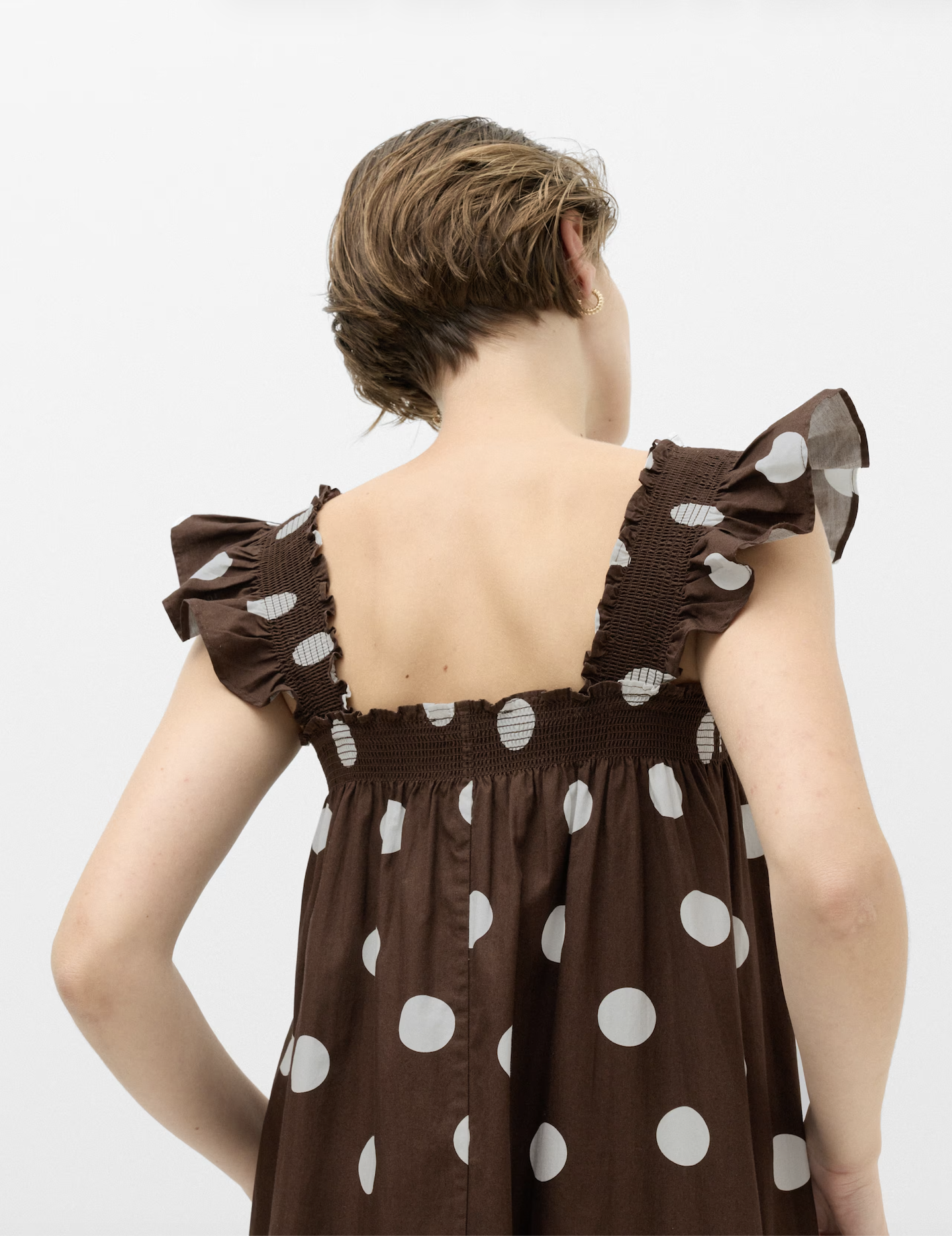 Back view of a woman with short brown hair wearing a brown polka dot dress with puffed sleeves.