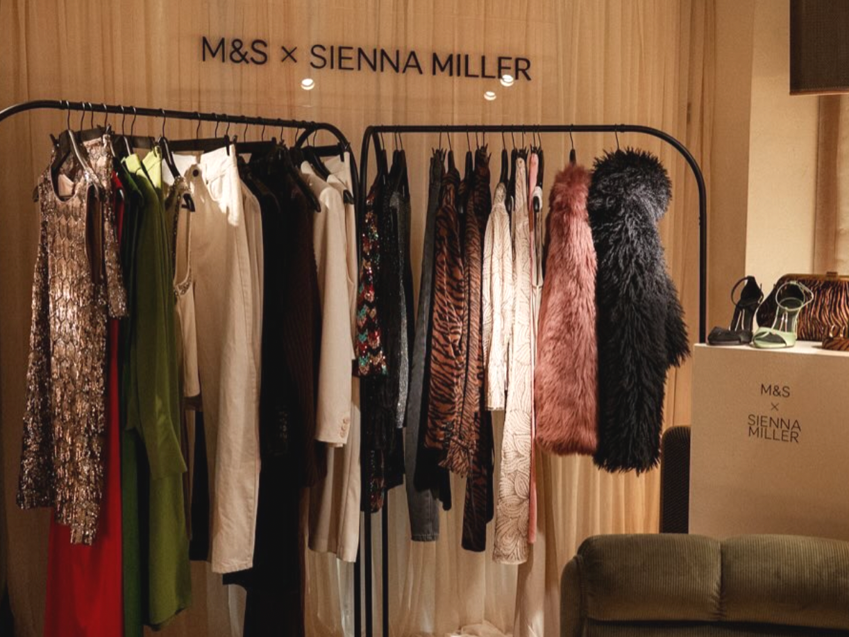 Clothing rack with dresses, jackets, and furry coats, with branding for M&S and Sienna Miller.