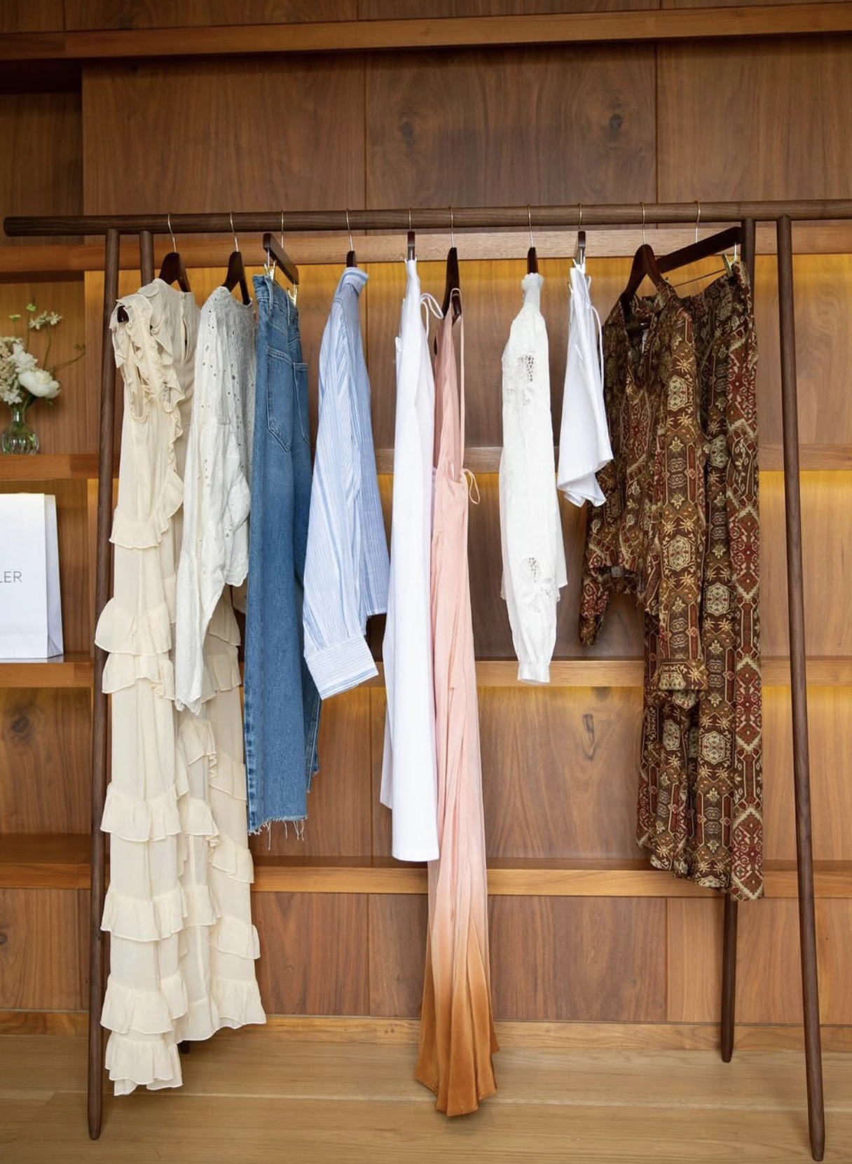 A wooden clothing rack with a variety of women's clothing, including dresses, tops, and pants, hanging on wooden hangers.